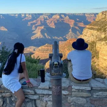 two people sitting on rock wall facing the grand canyon