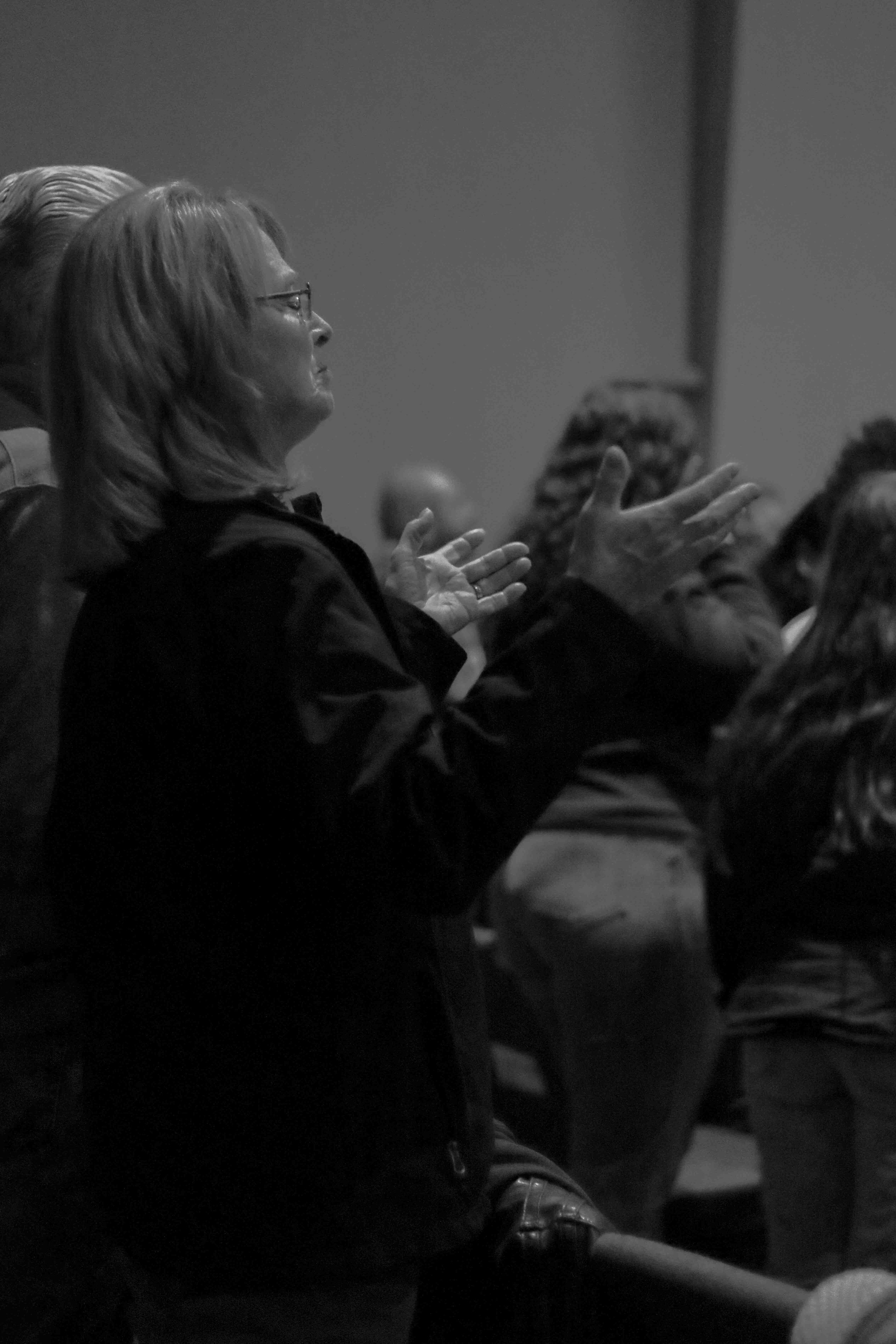 A woman with glasses and shoulder-length hair is clapping in a dark setting, possibly at a concert or event.