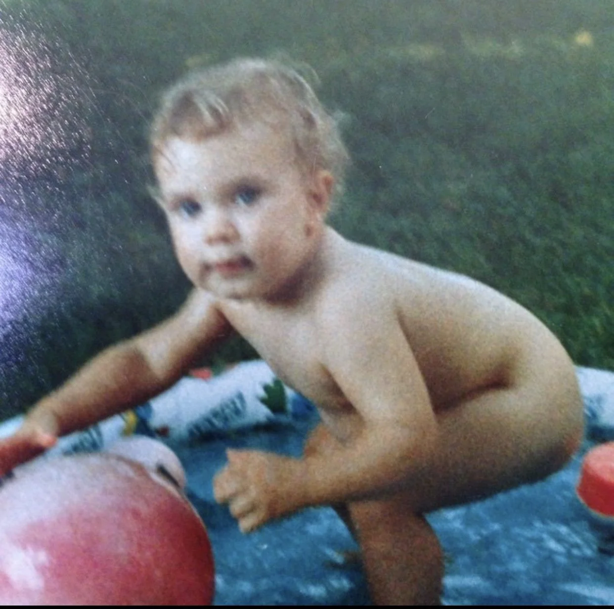 Toddler playing outside, standing near a toy, on a grassy area.
