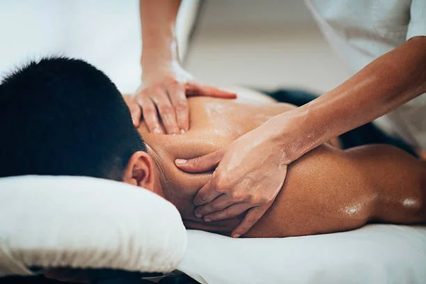 Person lying face down on a massage table receiving a back massage from a massage therapist.