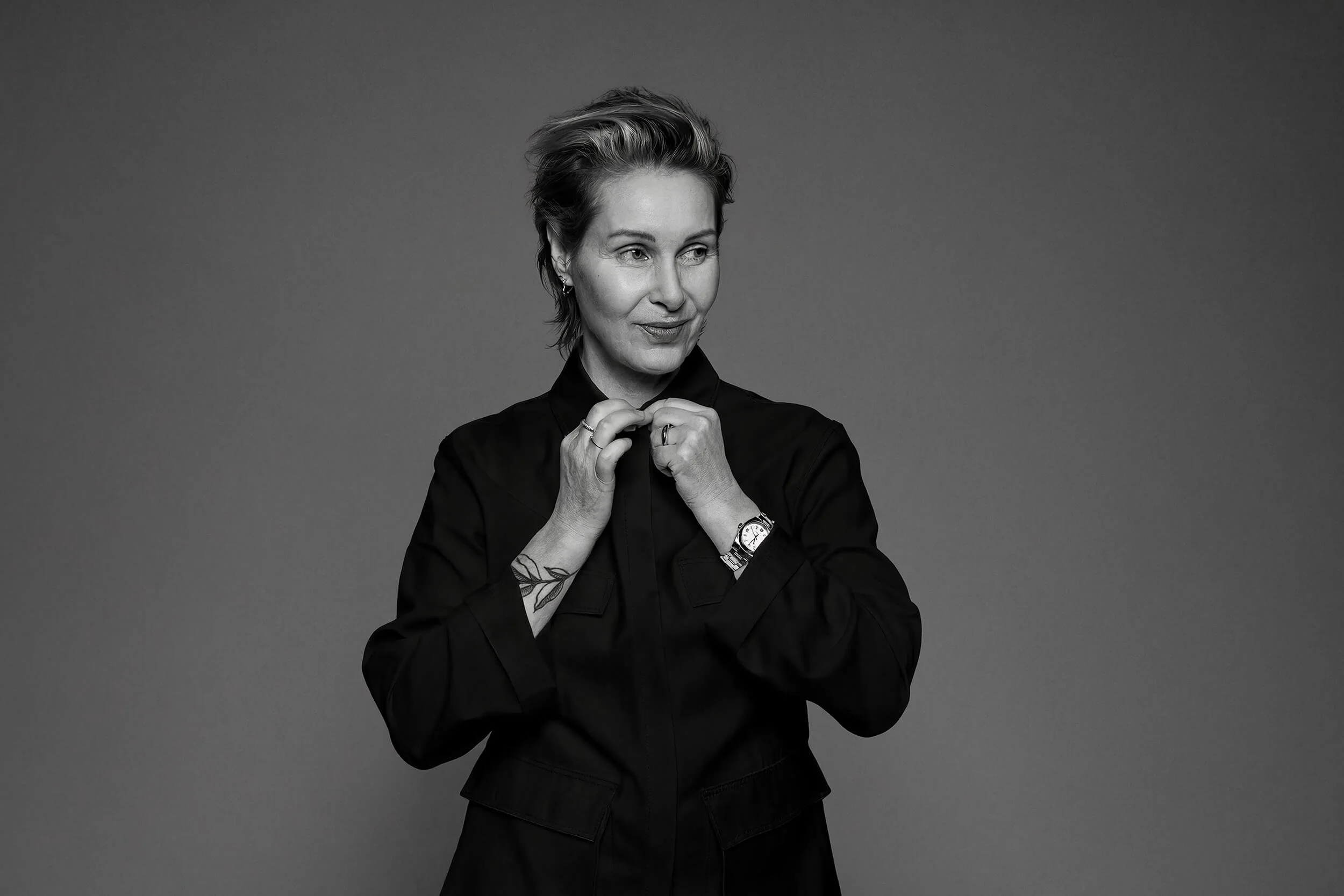 Black and white portrait of a woman with short hair, wearing a dark shirt, with her hands tucked under her chin and a gentle smile.