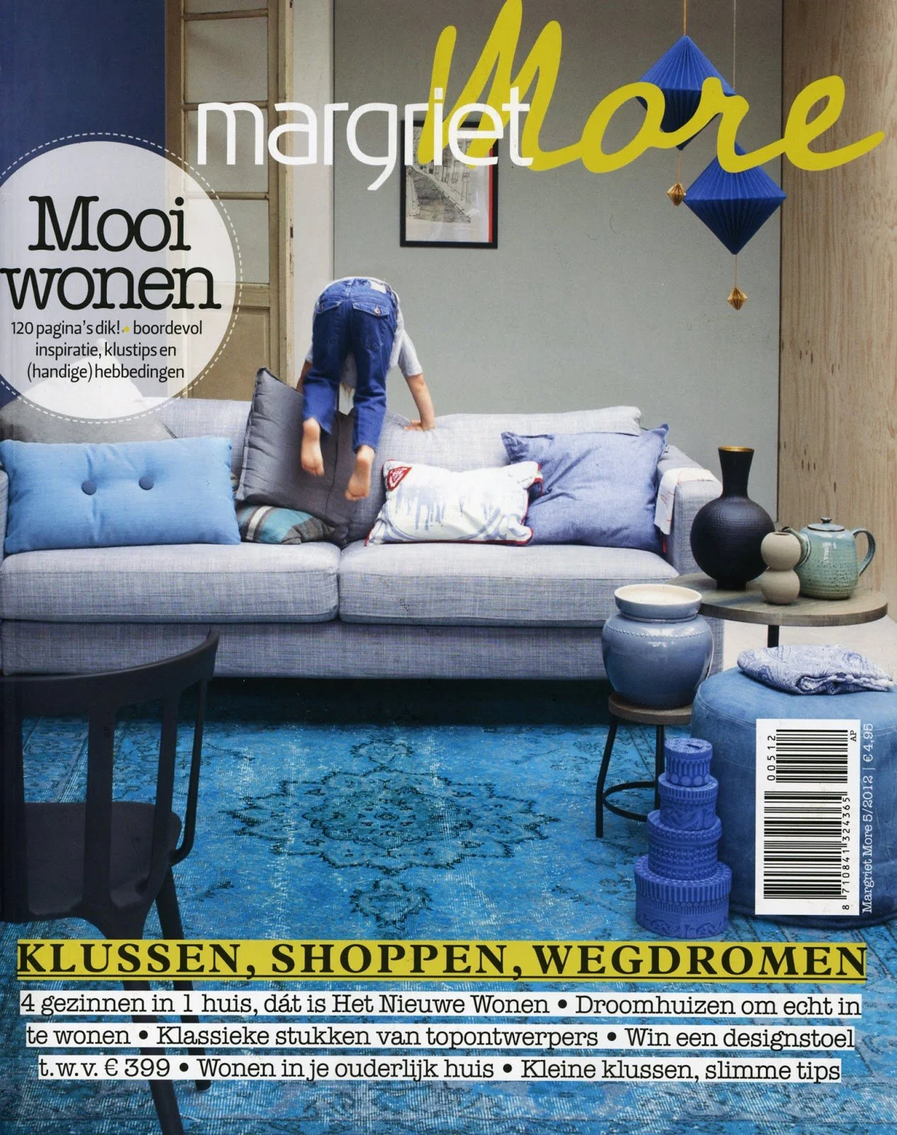 Cover of a magazine featuring a living room with a blue rug, a gray sofa with various pillows, a child climbing on the sofa, and decorative items including vases and lanterns. The magazine title is in large yellow and white letters, with additional t