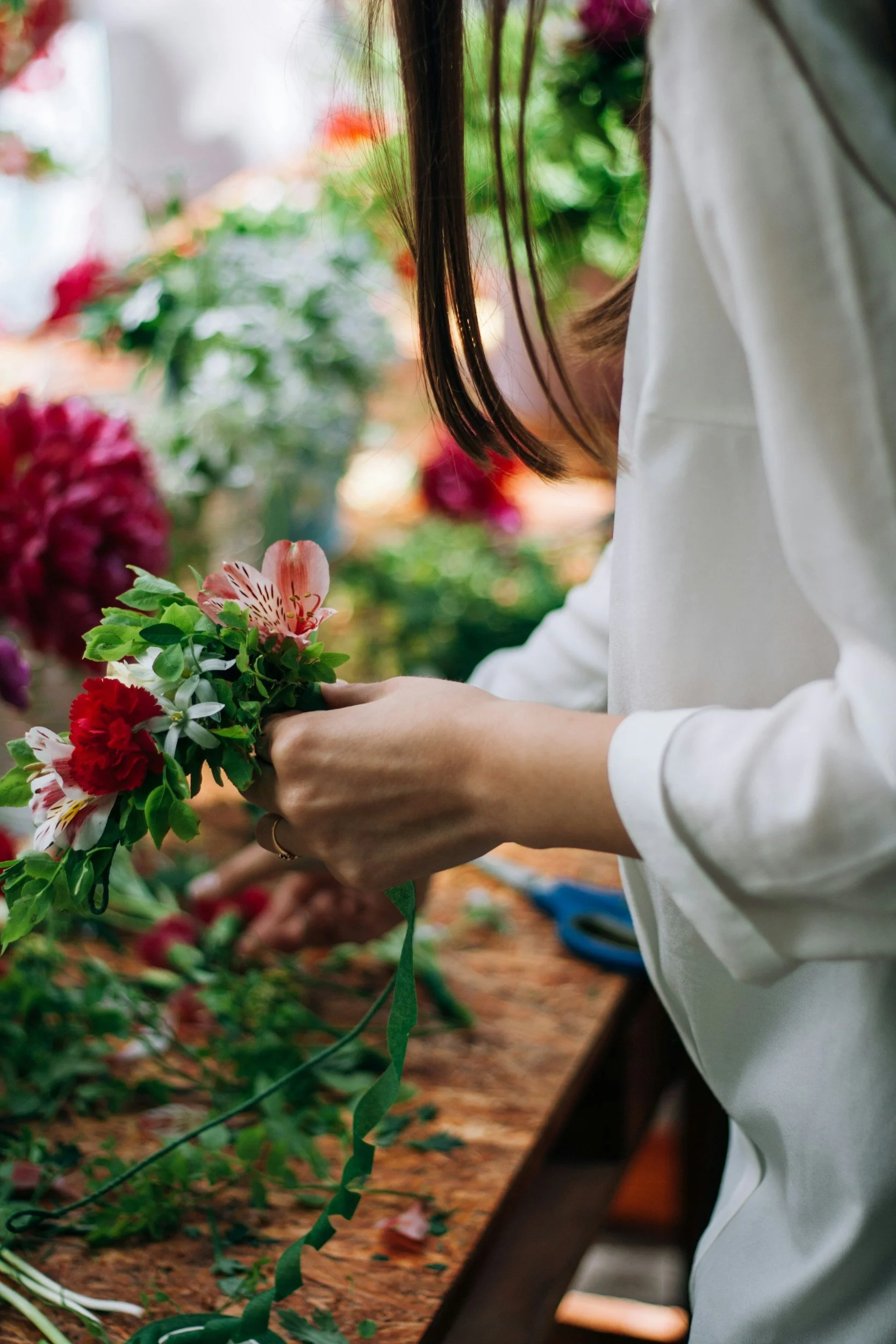 Person in white shirt arranging flowers in a floral shop or greenhouse.