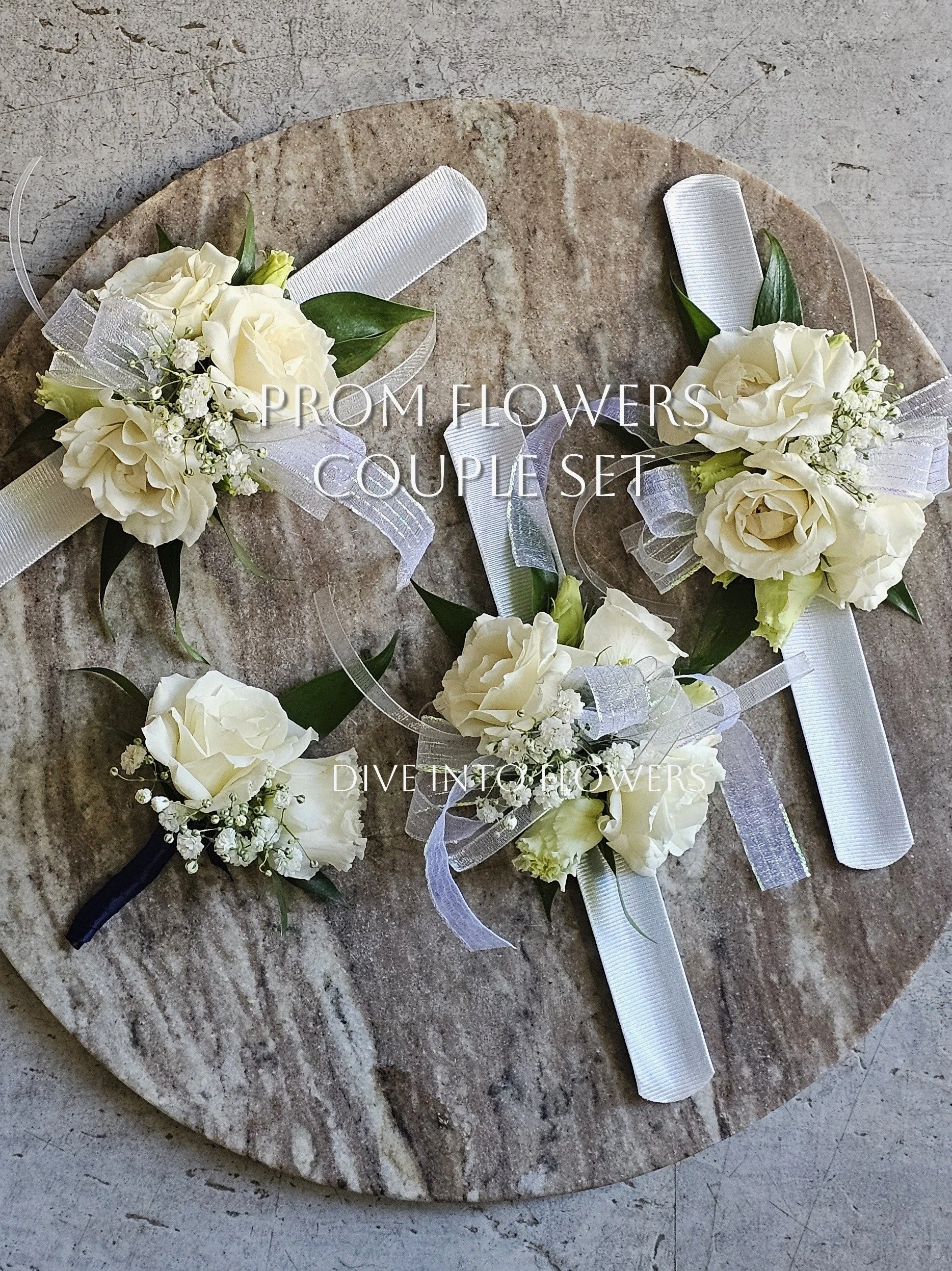 Prom Corsages, Boutonnieres & Graduation Bouquets Toronto | Dive Into Flowers. A set of corsage boutonnieres made of white flowers, green leaves, and white ribbon, arranged on a round stone surface.