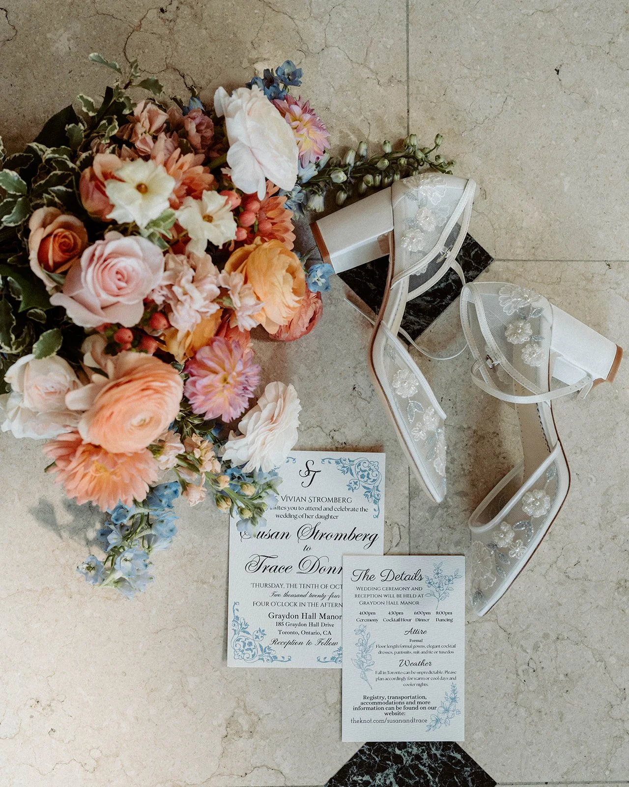 A bouquet of colorful flowers next to wedding invitations and a pair of white embellished sandals on a tiled floor.