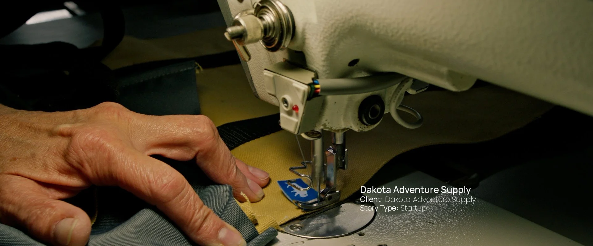 Close-up of hands sewing canvas gear on an industrial machine, still from a Passenger Productions startup documentary for Dakota Adventure Supply