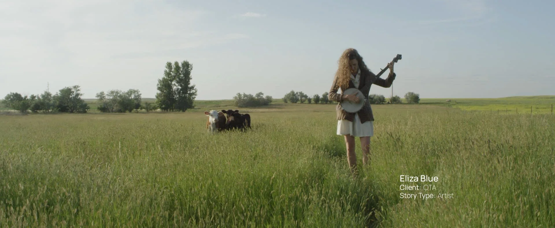Musician Eliza Blue playing banjo in a South Dakota prairie field with cattle, still from a Passenger Productions artist documentary