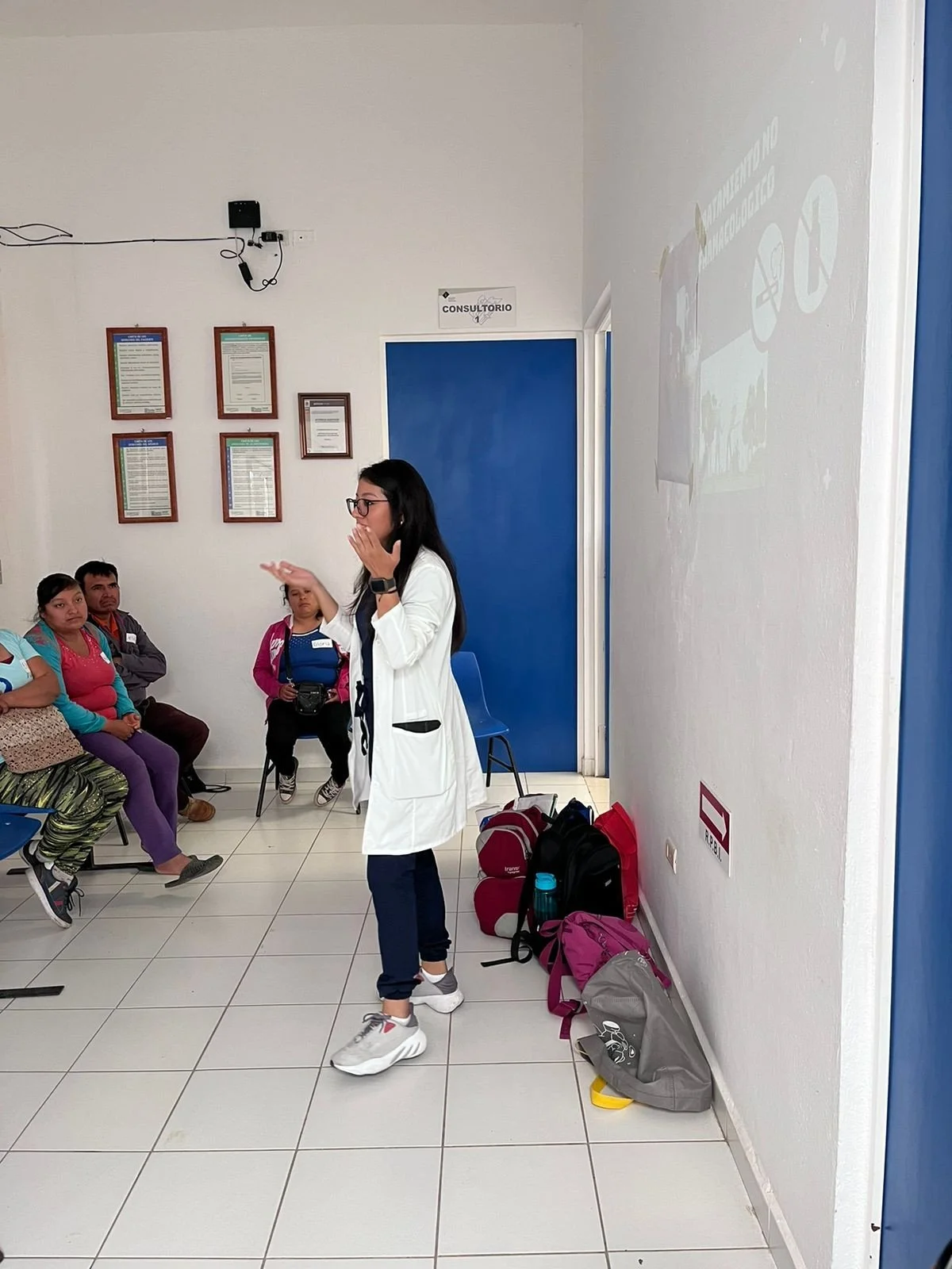Woman in a white coat talking to people in a classroom