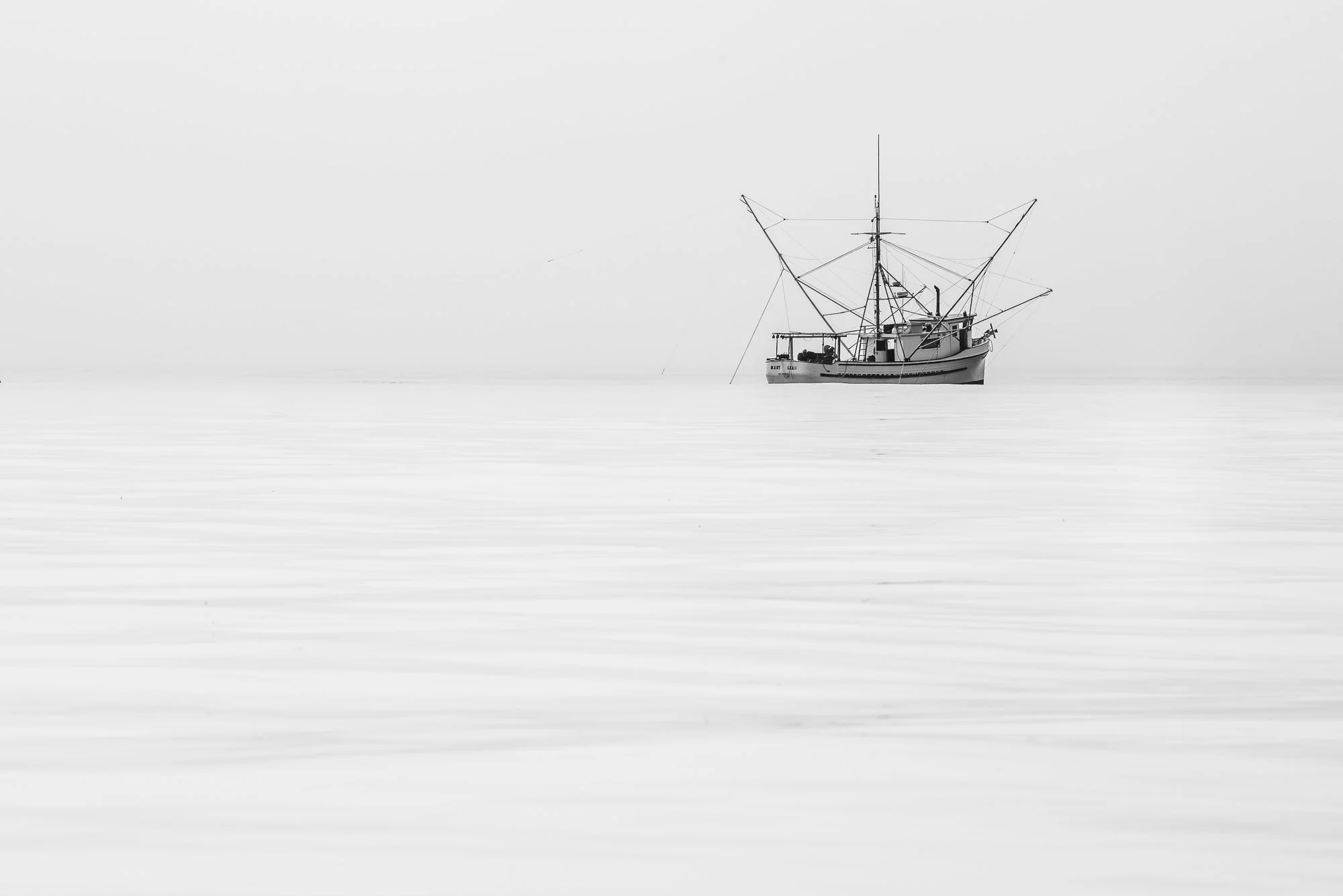 A lone salmon fishing vessel sits on calm water during a foggy morning in Monterey Bay, California.
