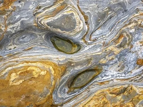 Fine art abstract rock pattern photographed by Jason Bradley in Pacific Grove, featuring swirling gray, gold, and white mineral layers with tide pool formations.