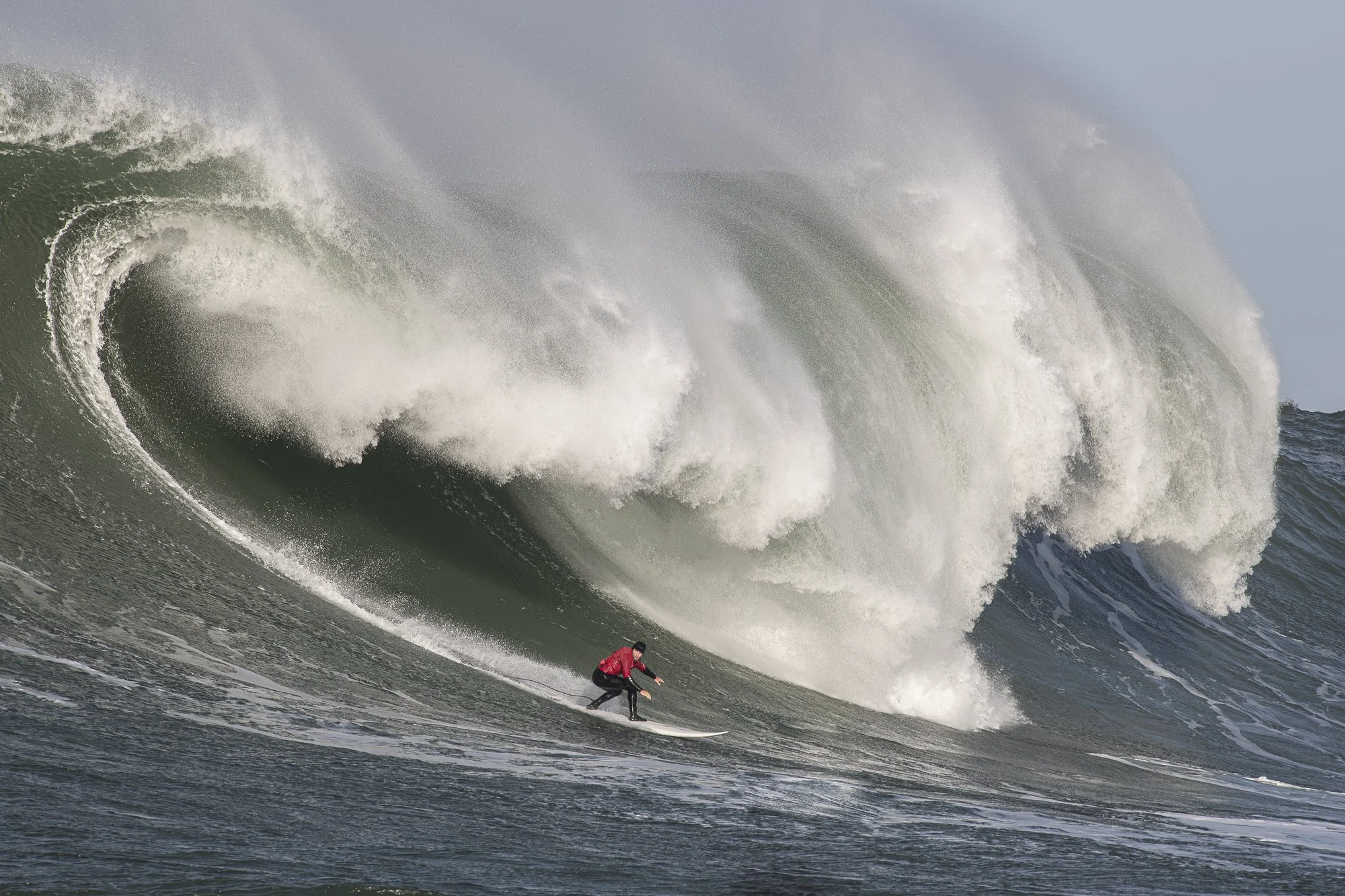 Surfer riding beneath a massive breaking wave at Mavericks in Northern California.