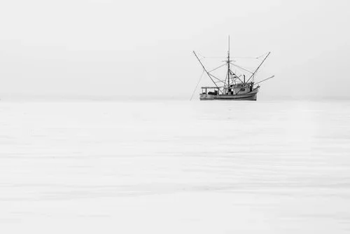 Black and white high key photograph of a lone salmon trawler on calm waters in Monterey Bay at sunrise, by Jason Bradley.
