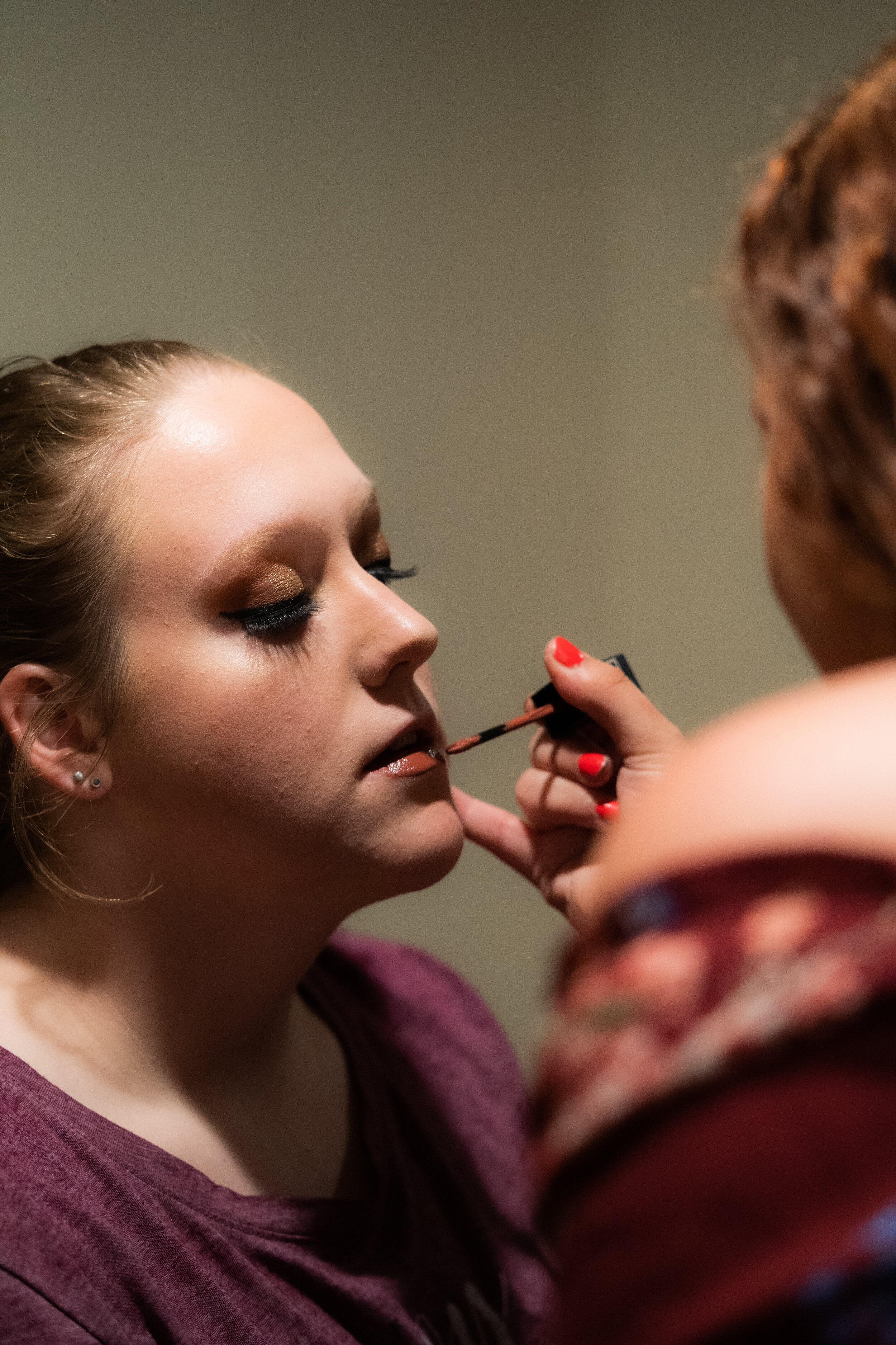 A woman getting her makeup done by a makeup artist, who is applying lipstick.