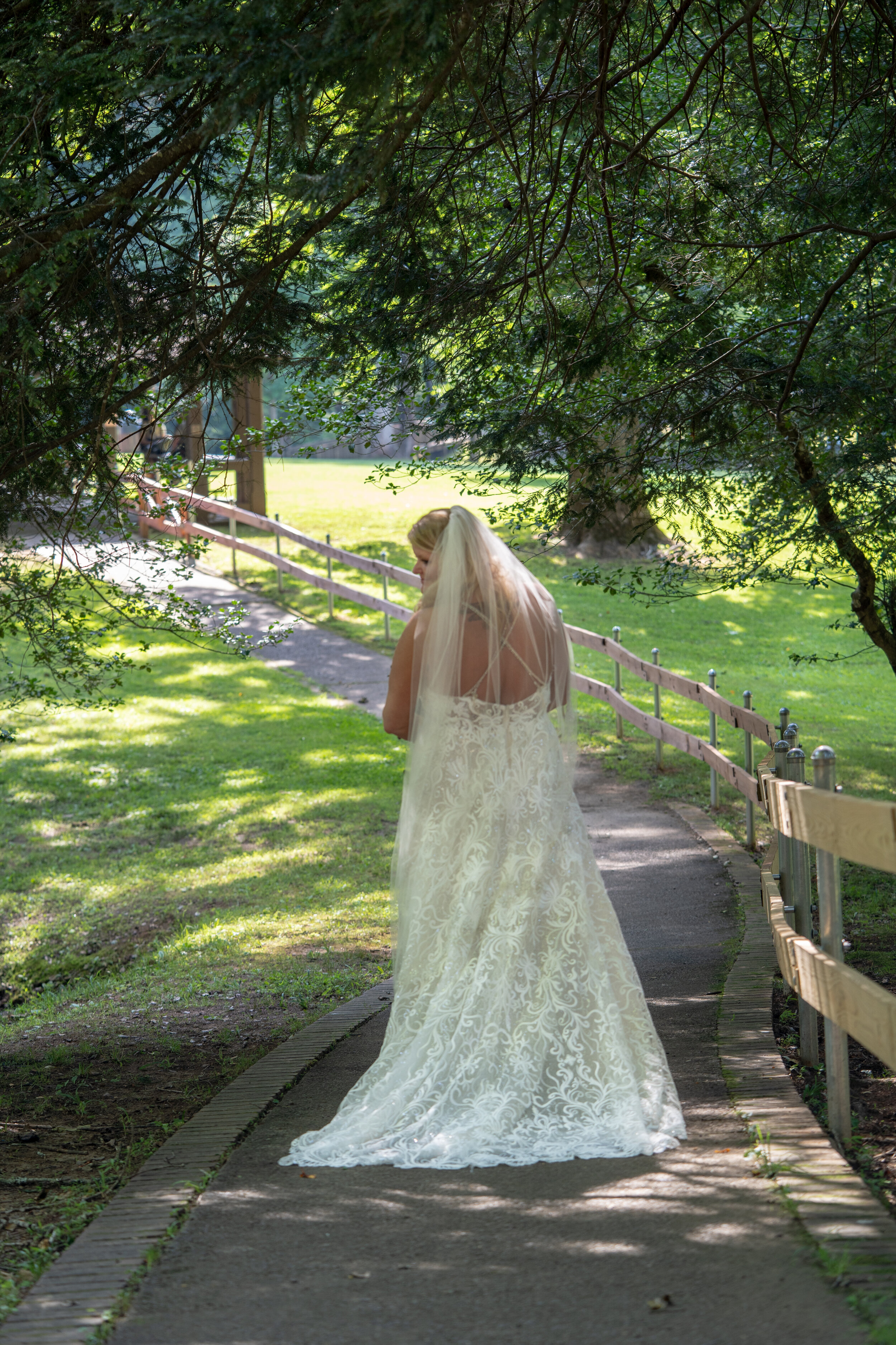 Bride in a white wedding gown with a veil walking on a park pathway surrounded by greenery.