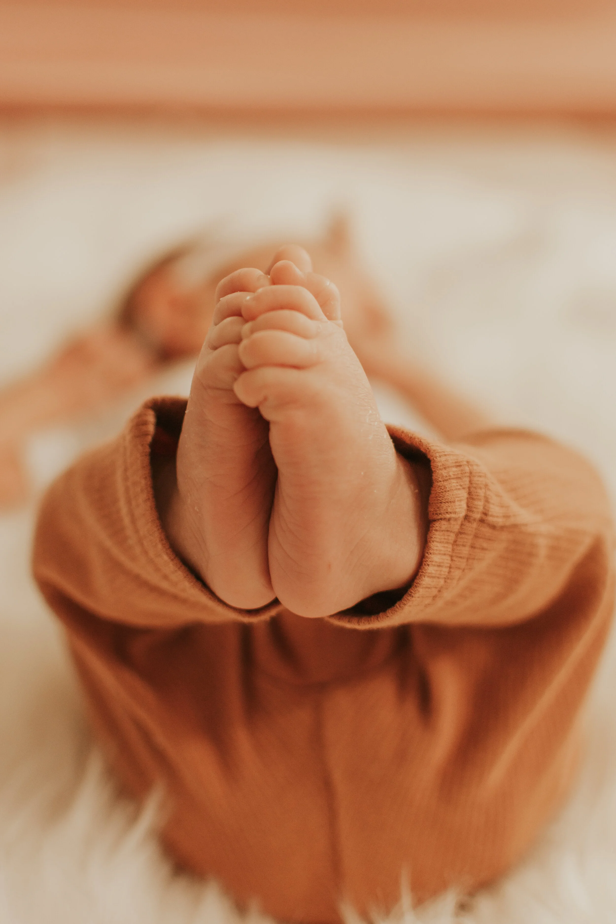 A newborn baby girl holds her feet and curled toes in the air during an in home photoshoot.