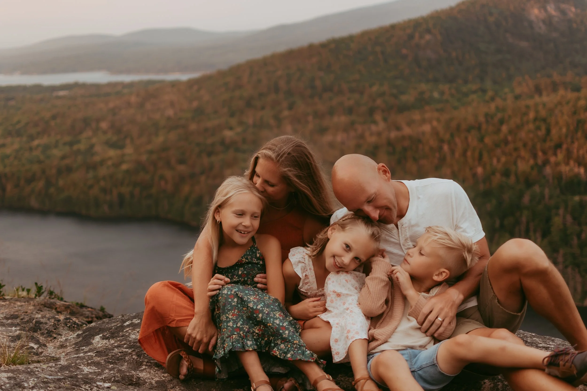 A loving family cuddles up on one of Acadia's ledges, overlooking the mountains and water. 