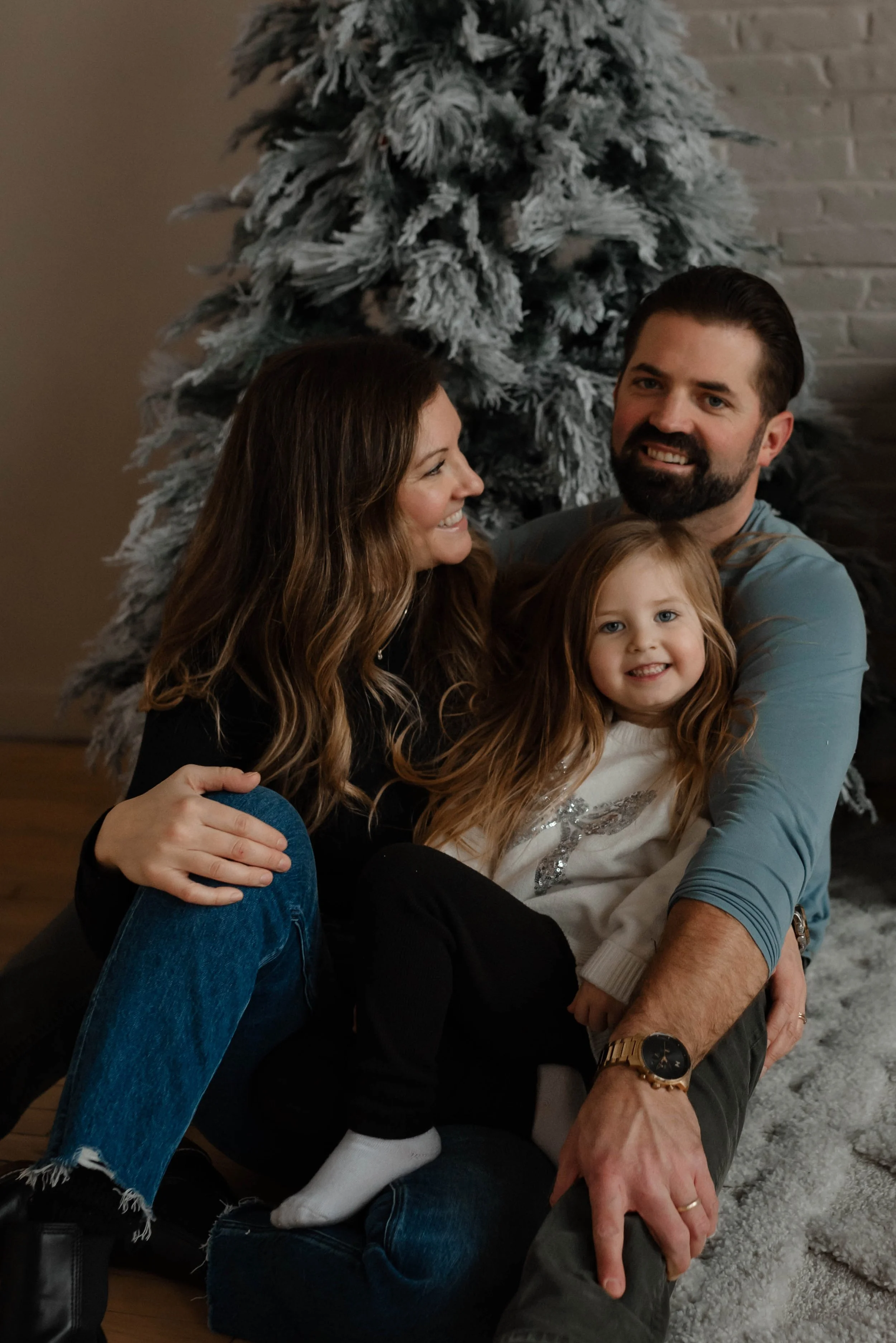 A young family snuggles close in front of a Christmas tree during their family photos.