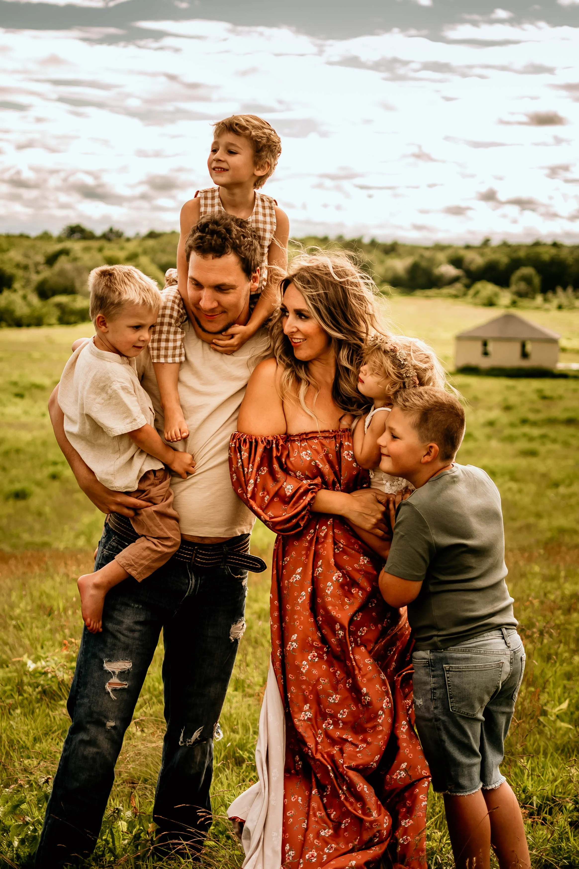 Dad holds one son on his shoulders with another in his arms, as Mom and the oldest son snuggle into the only baby girl during a Maine family photoshoot.