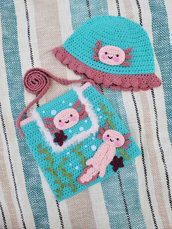 Crocheted blue and pink hat and matching bag with cute axolotl designs on a striped background.