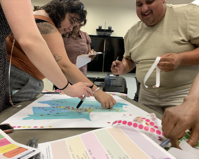 People collaborating around a table with a large map and colorful stickers, engaged in a group activity.