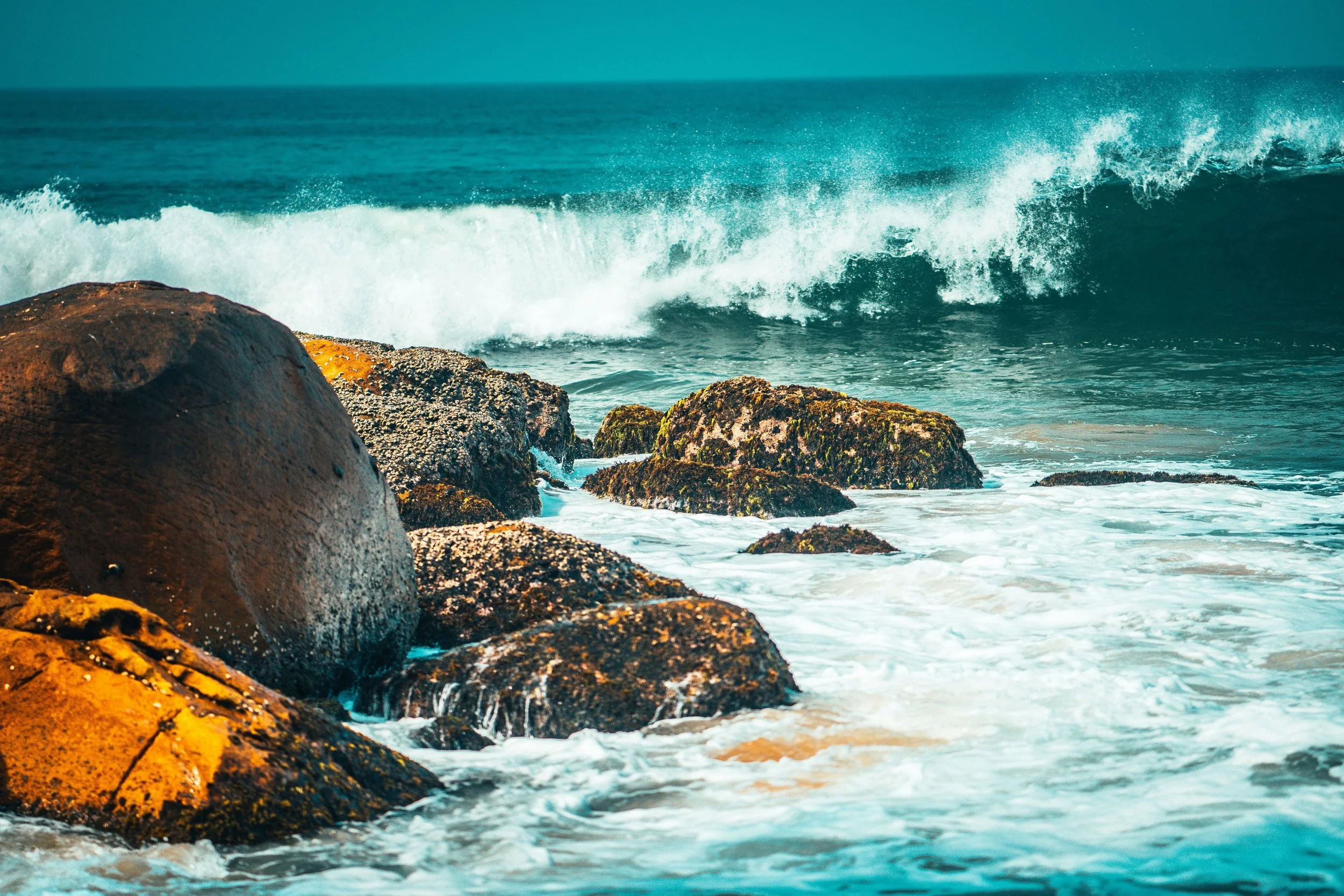 Ocean waves approaching brown rocks