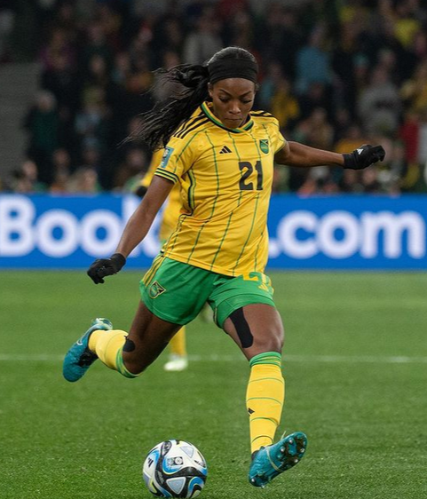 Cheyna Matthews, a former soccer player in yellow jersey and green shorts kicking a soccer ball on the field.