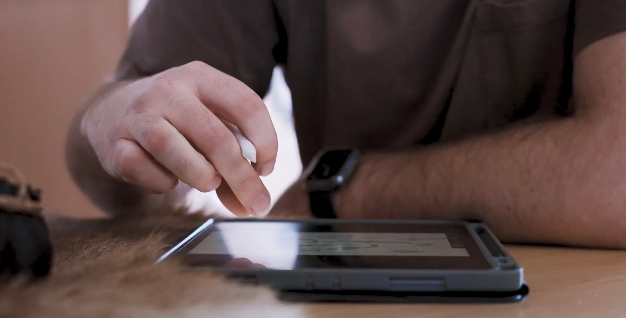 Hand holding a white stylus above an iPad during digital illustration.