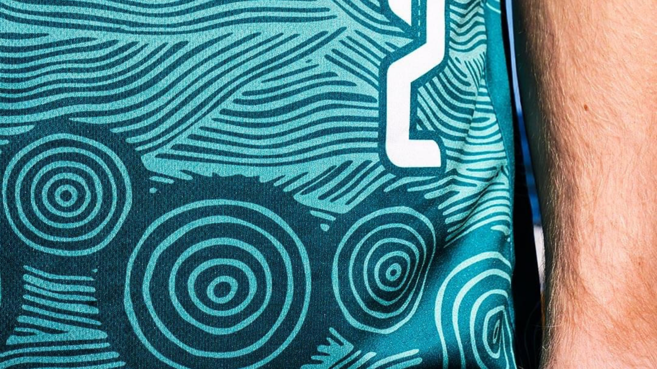 Detail of the Indigenous Round jersey showing circular motifs, flowing teal linework and a white player number.