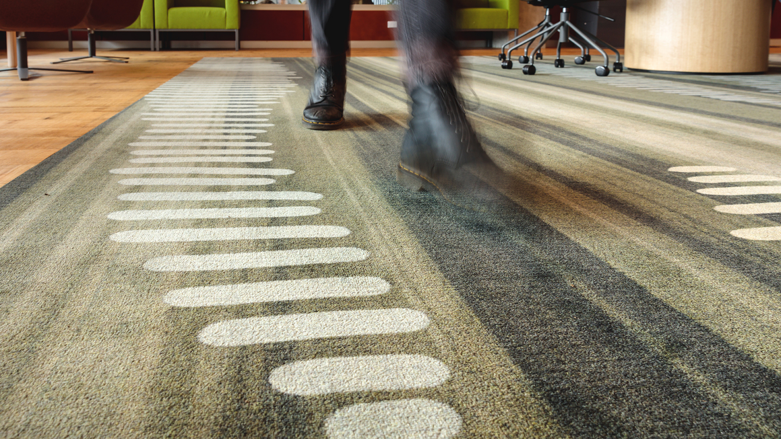 Close-up of Wetlands II, showing cream reed forms on a green-grey carpet as a visitor walks through UTAS Inveresk Library.