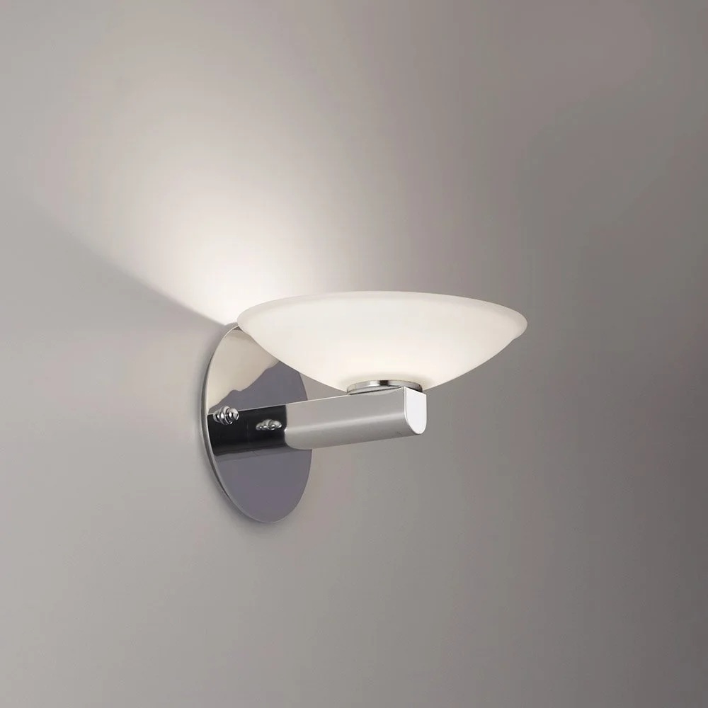 modern polished chrome & glass sconce illuminated on a wall with a round mounting plate