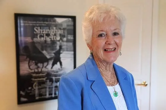 Betty Grebenschikoff at home in Florida, in front of the poster for the documentary Shanghai Ghetto