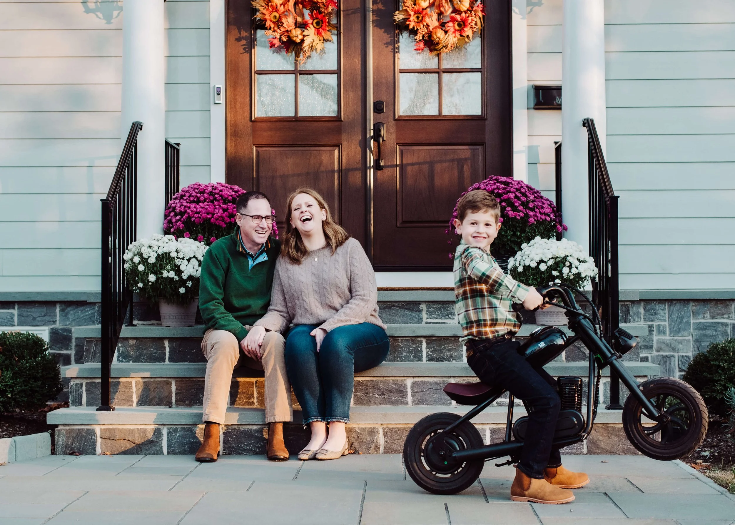 A family of three sitting in front of the house with a bicycle 