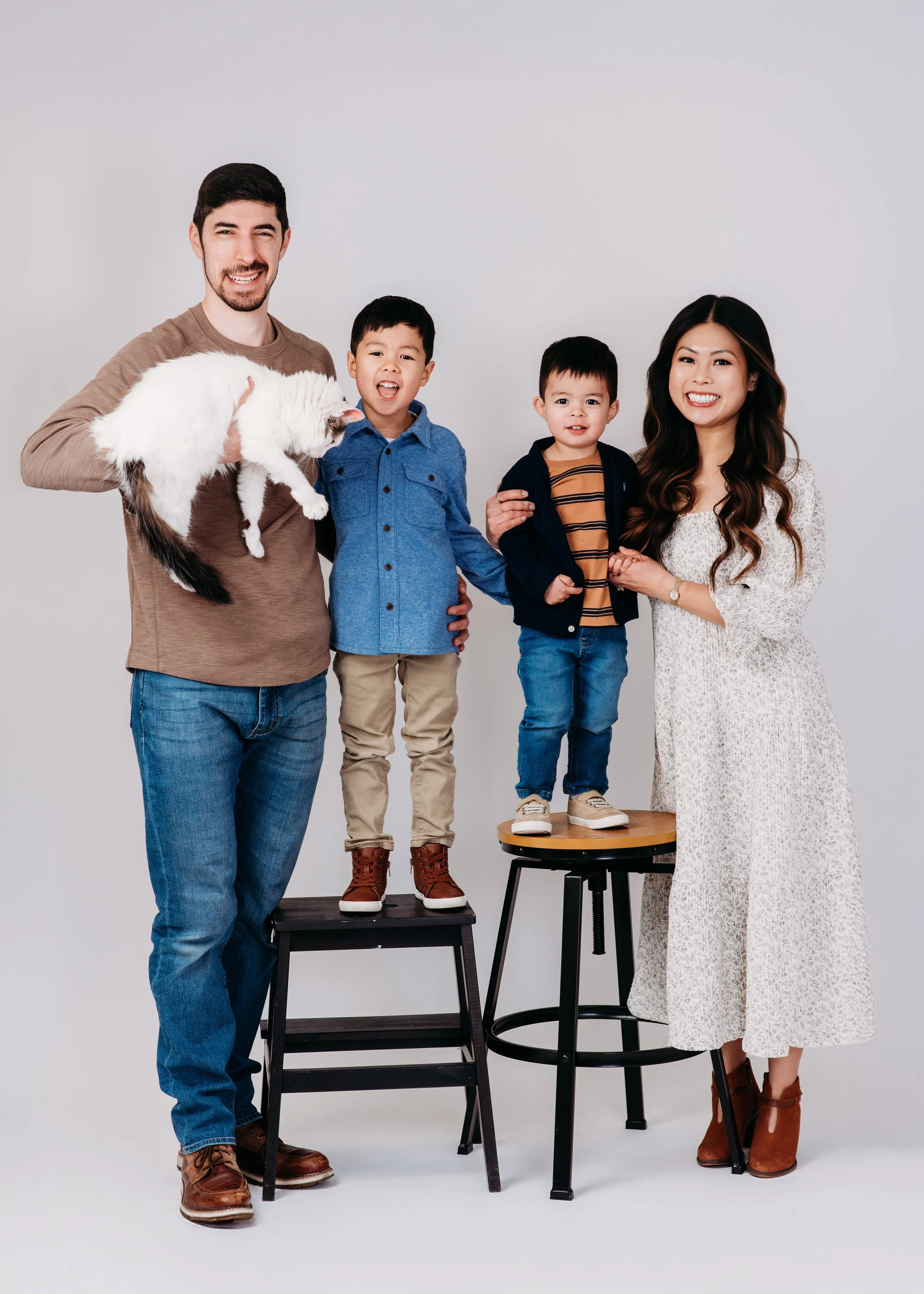 A happy family of four with two children, one holding a white and black cat, standing against a plain gray background.