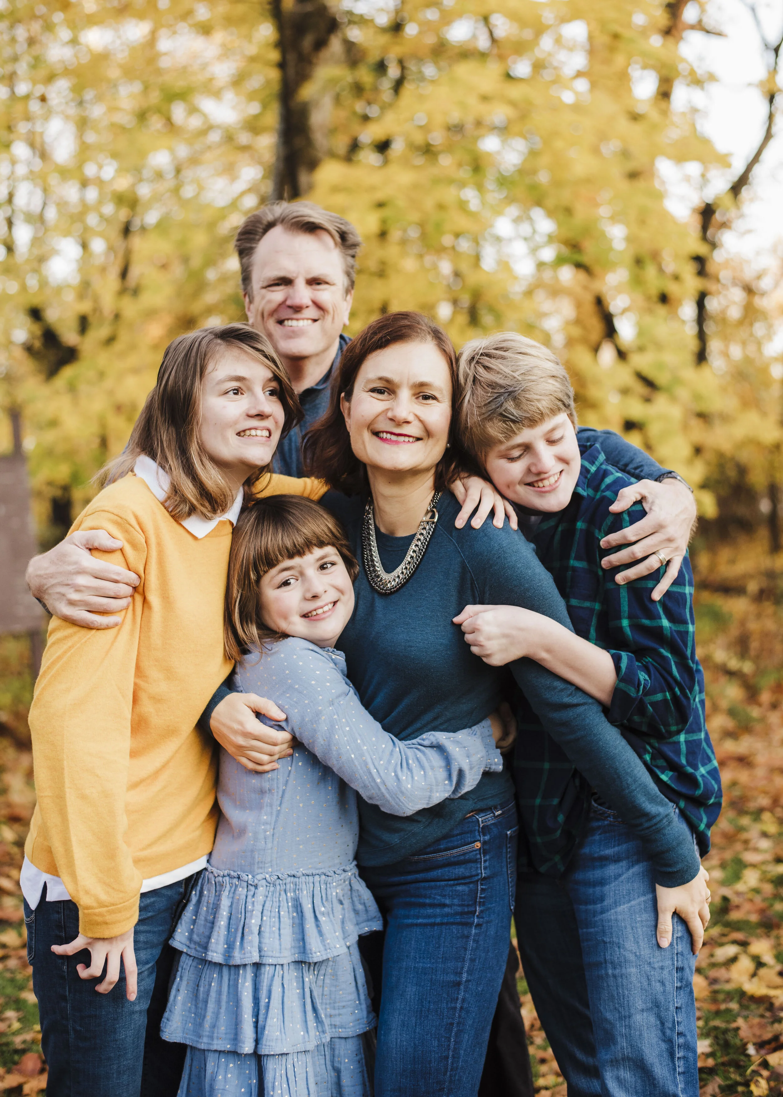 Family of five hugging each other with yellow leaves in the background
