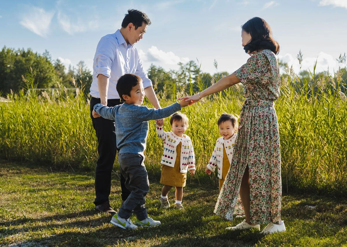 A family of five playing in a field on a sunny day, with children and adults smiling and interacting.