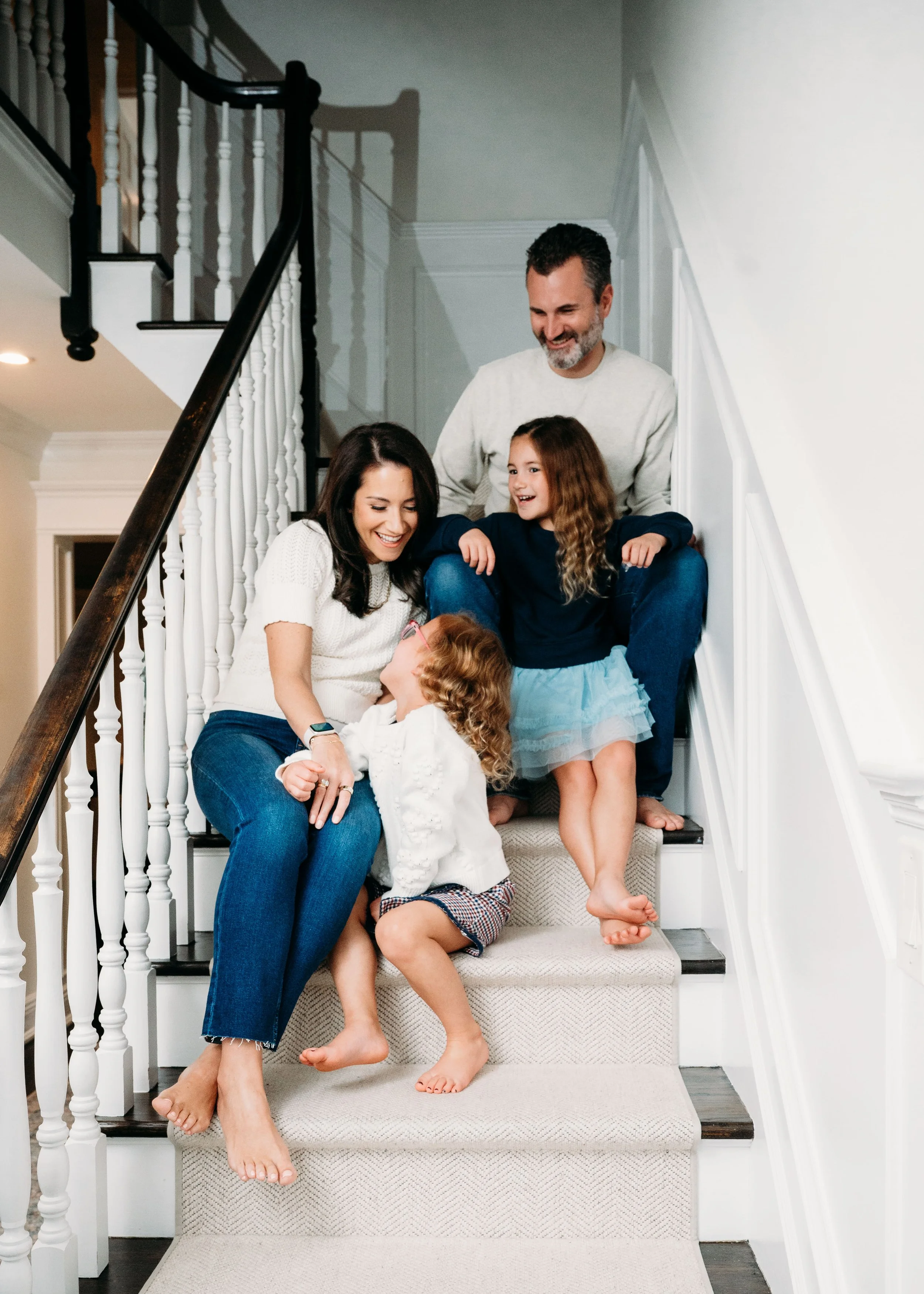 A family of five sitting on a staircase, smiling and interacting with each other at home.