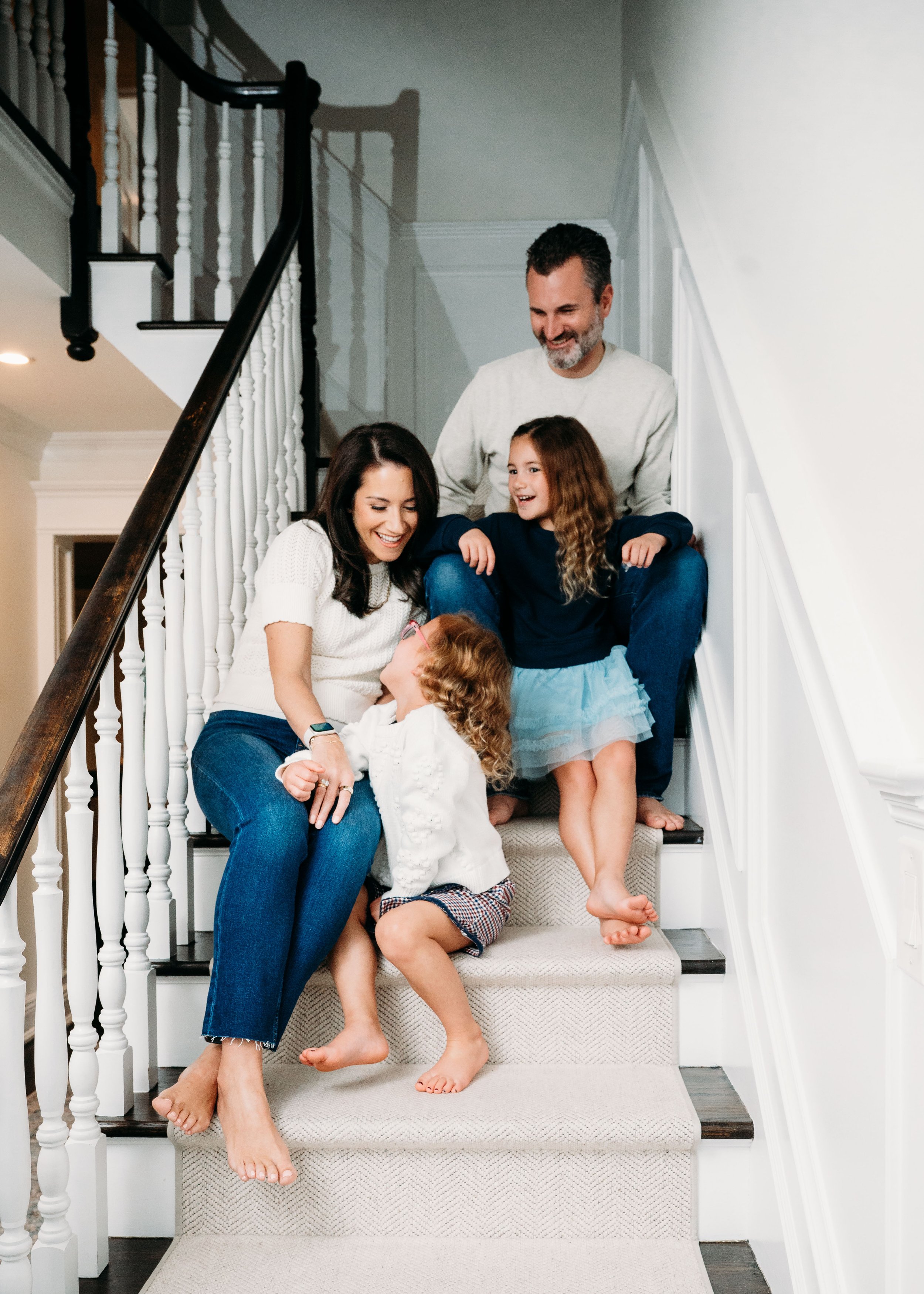 A family of five sitting on a staircase, smiling and interacting with each other at home.