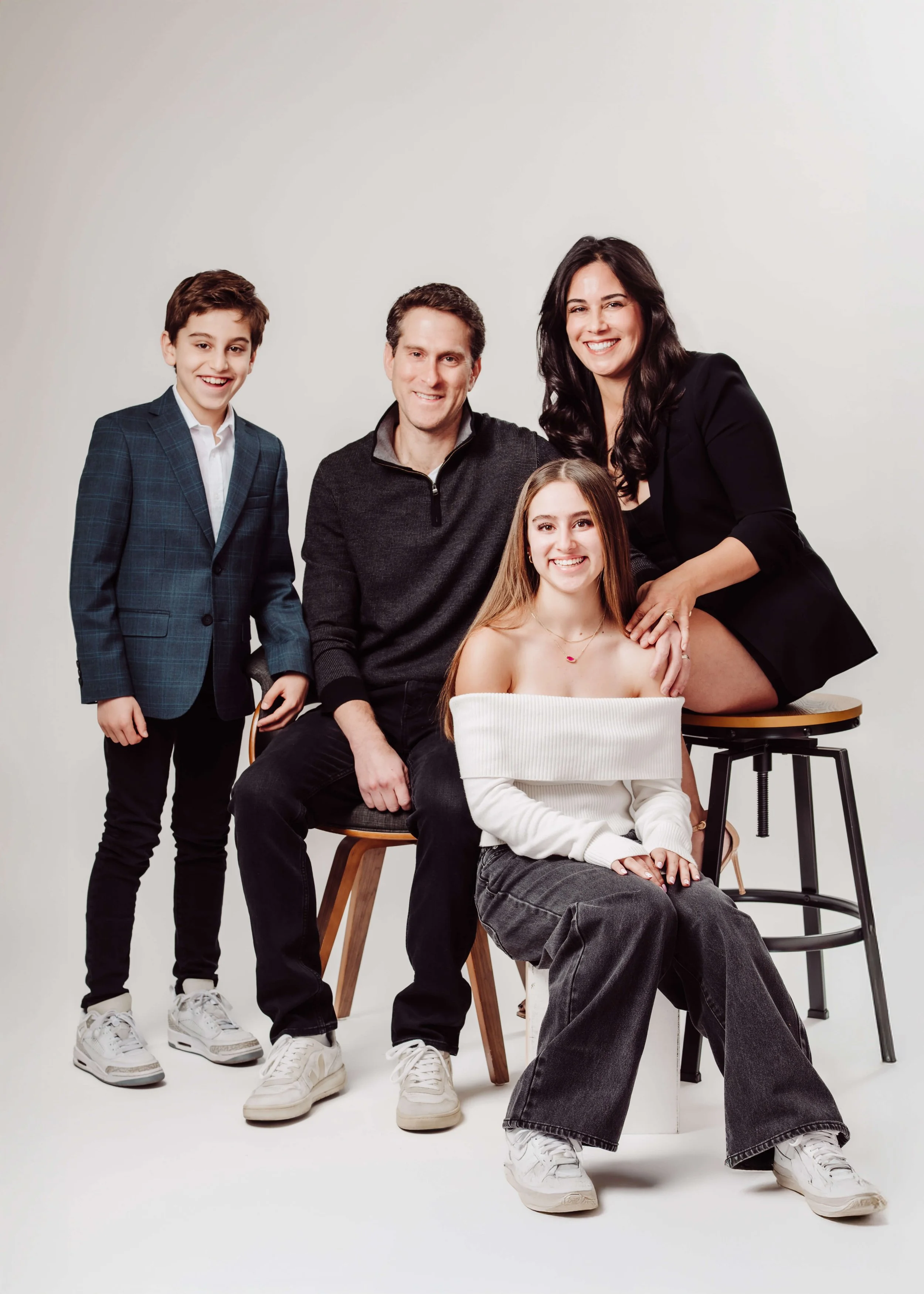 A family of four posing together against a white background, with two women, two men, and one boy, all smiling.
