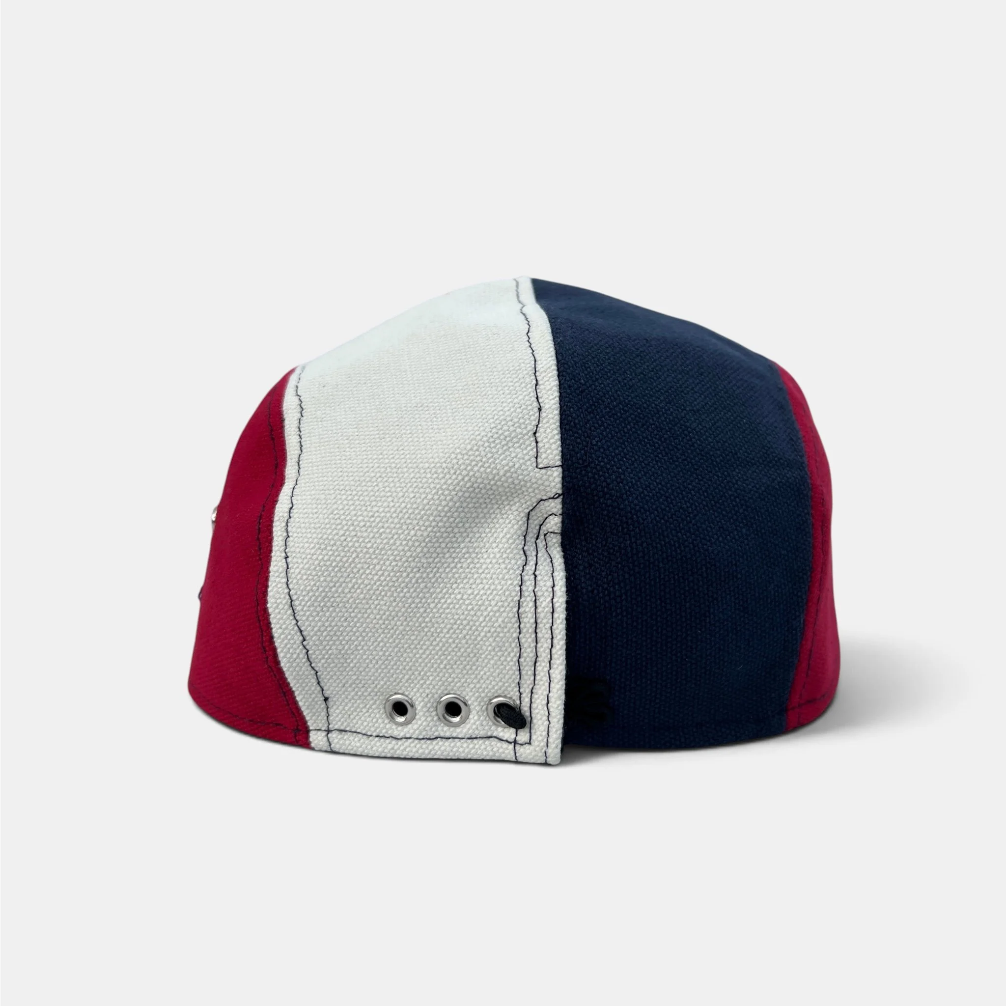 Back view of red, navy and off-white cotton canvas five-panel cap with adjustable closure and metal eyelets.