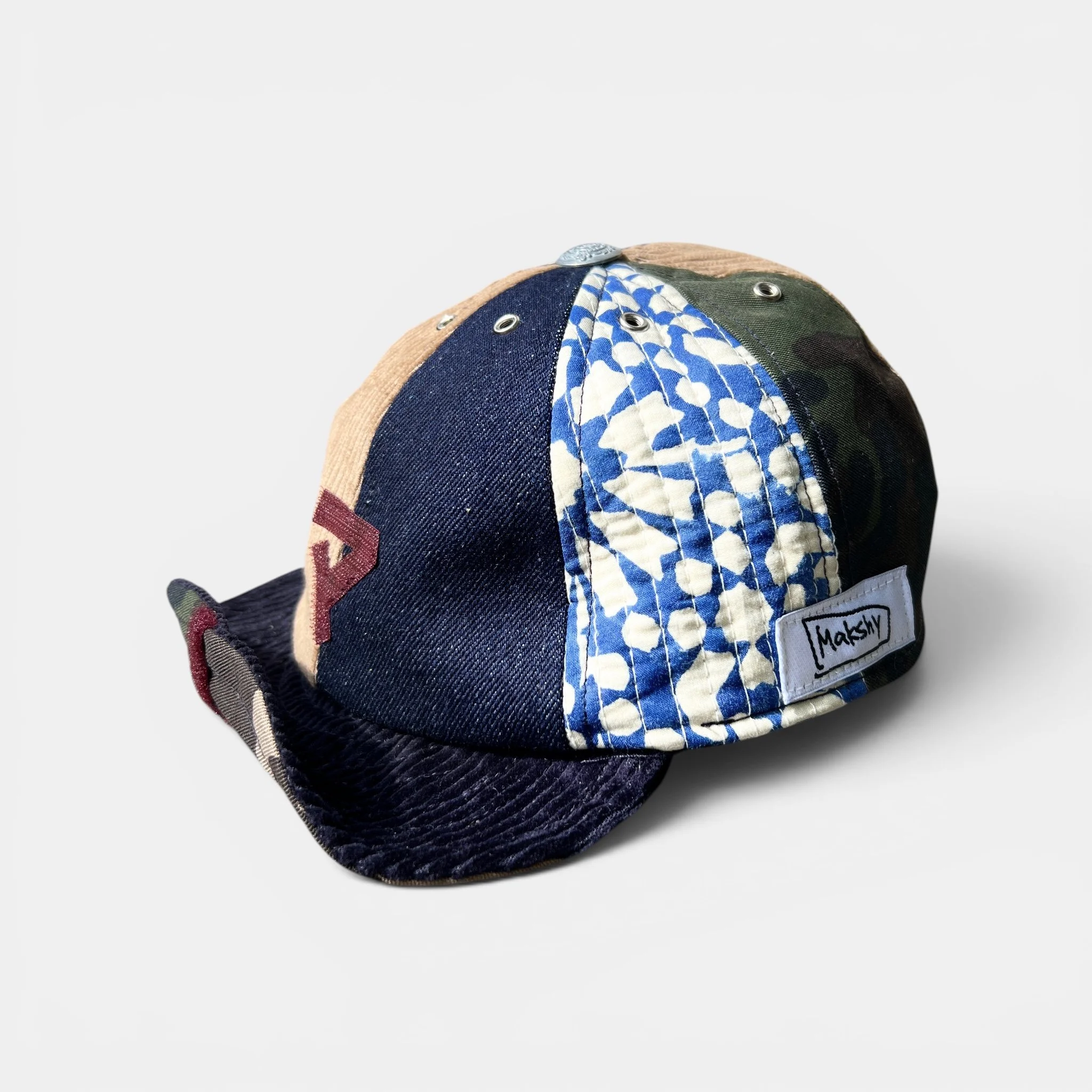 Dark mixed-panel cotton cap shown from the side, with deep navy, beige corduroy, camouflage and blue-and-white quilted cotton panels.