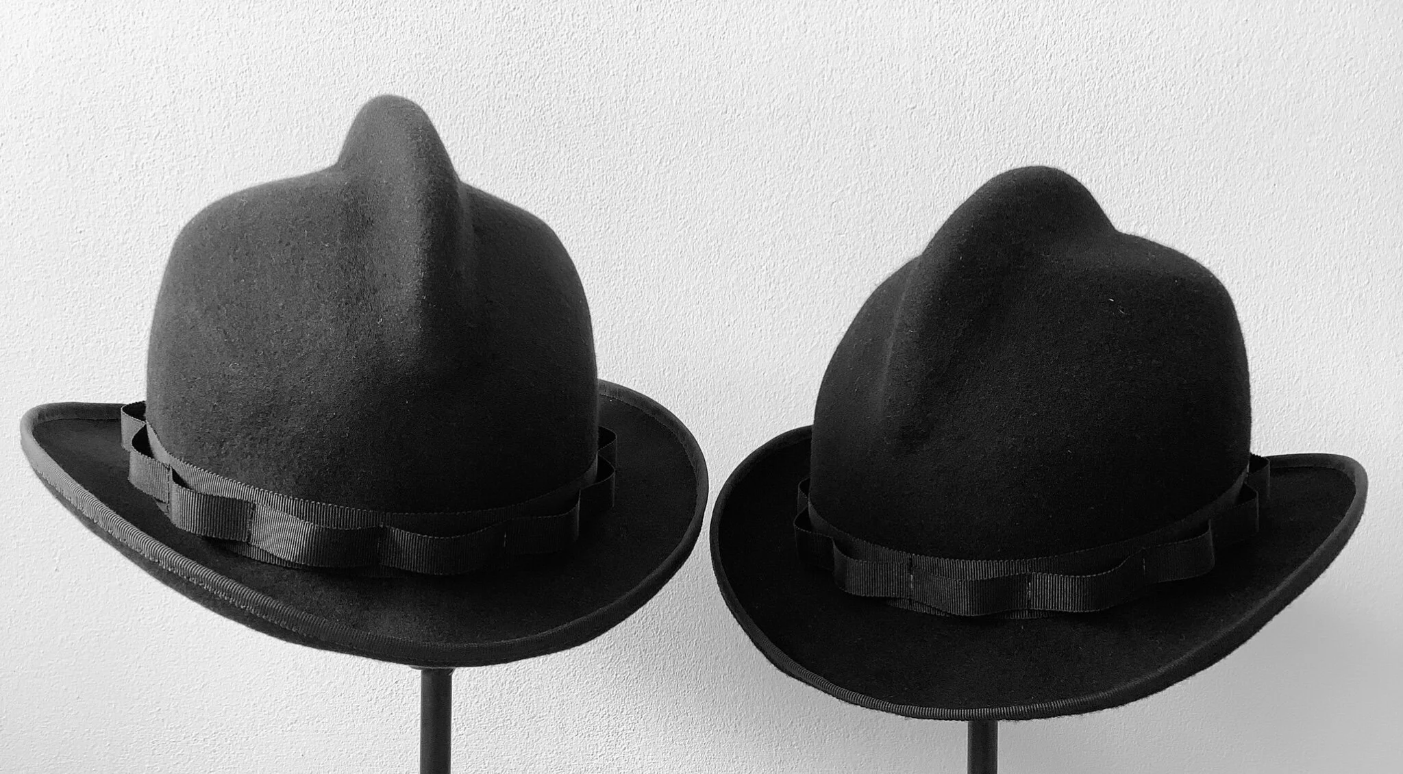 An artistic, minimalist shot showcasing the unique design of the Makshy Mohican Crown hat. Two of the hats are presented as a symmetrical pair in black and white, highlighting their bold, graphic shape.