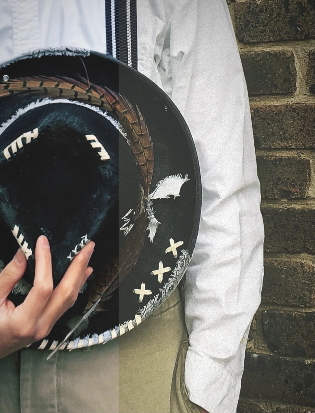 A close-up of a wearable art piece from Makshy Millinery: a black fedora-style hat, custom-painted with white markings and decorated with a full band of natural pheasant feathers.