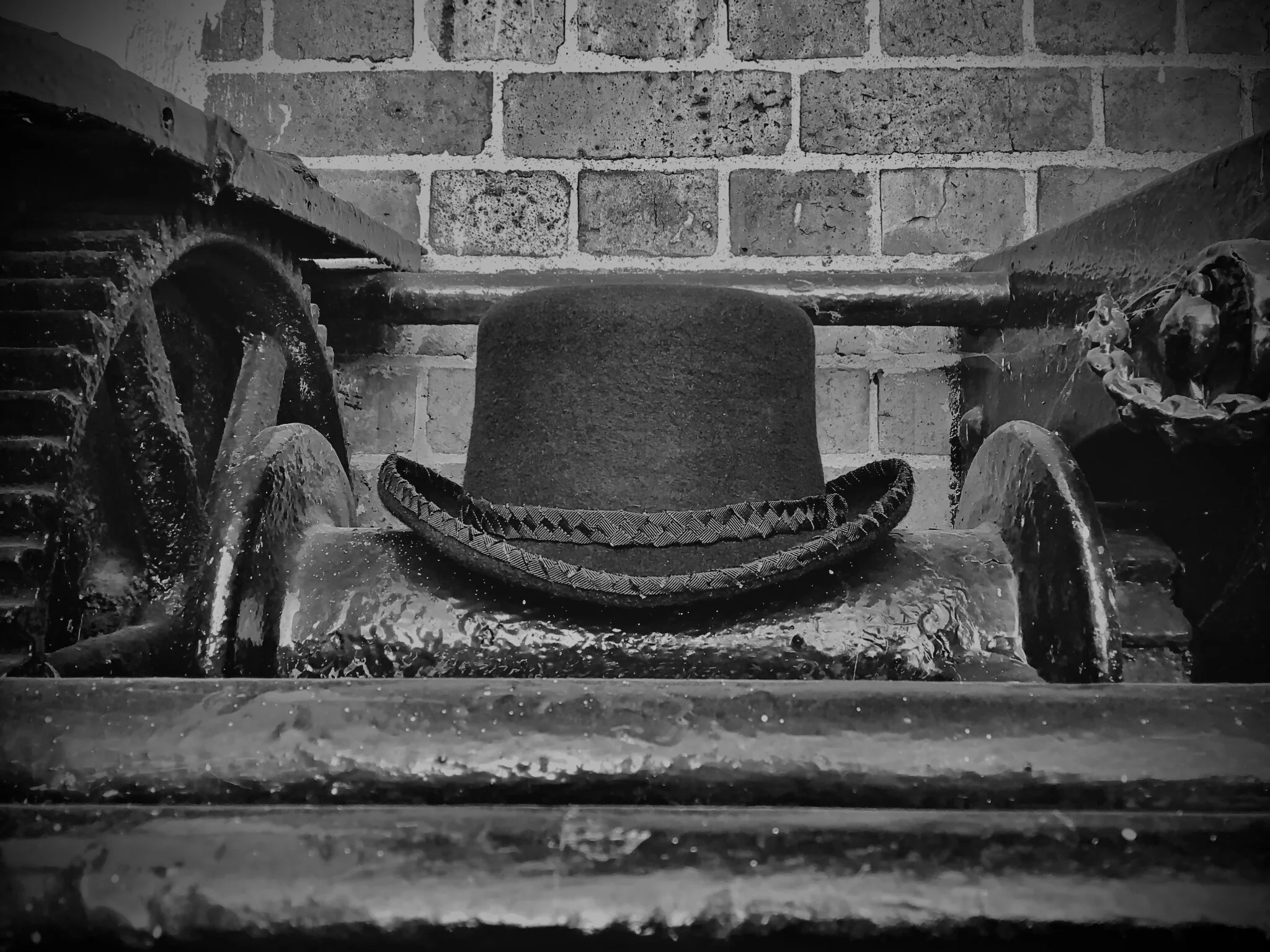 Evoking a powerful, industrial-era aesthetic, a Makshy bowler hat sits centrally on a cast-iron machine. The black and white image contrasts the soft felt of the hat with the hard, aged metal and rustic brickwork.