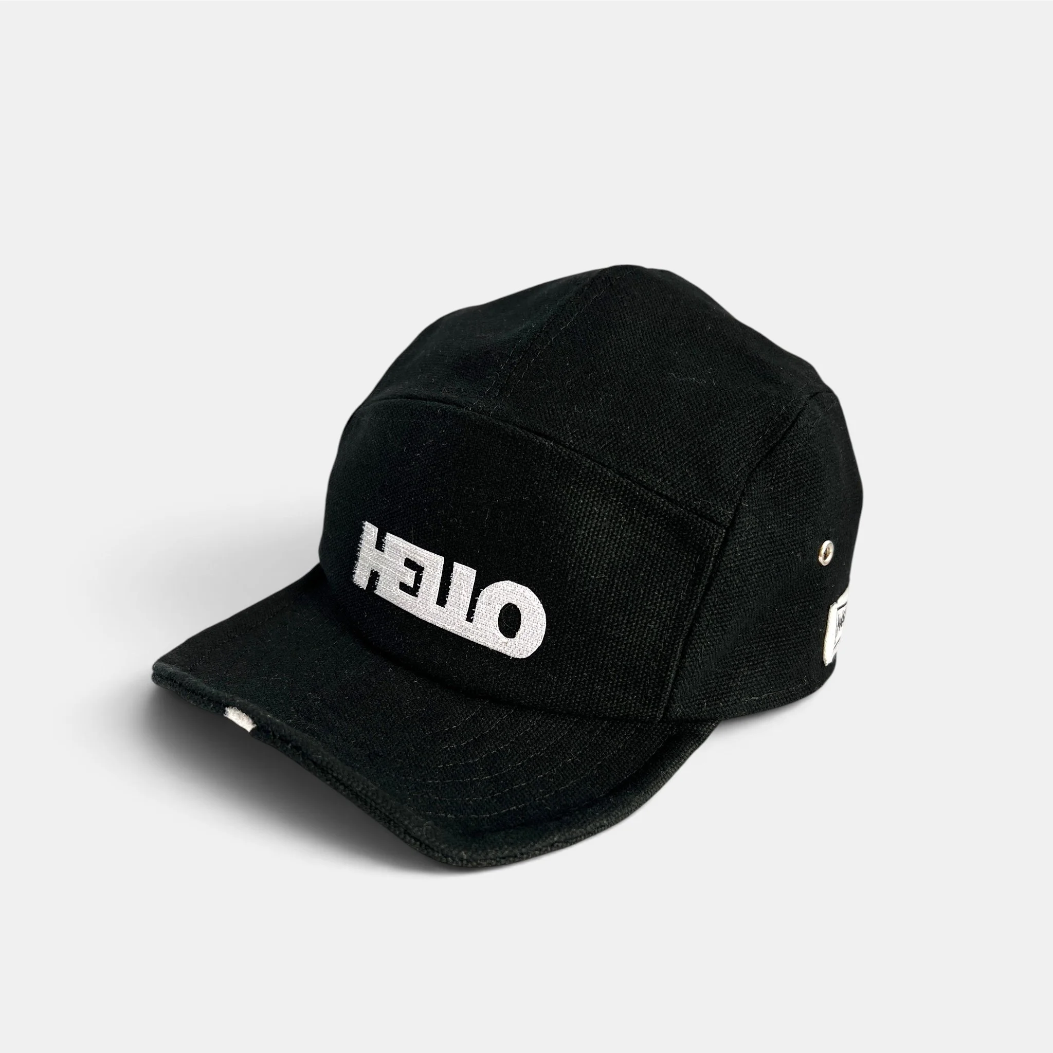 Black canvas five-panel cap with white HELLO motif and flat wired visor.