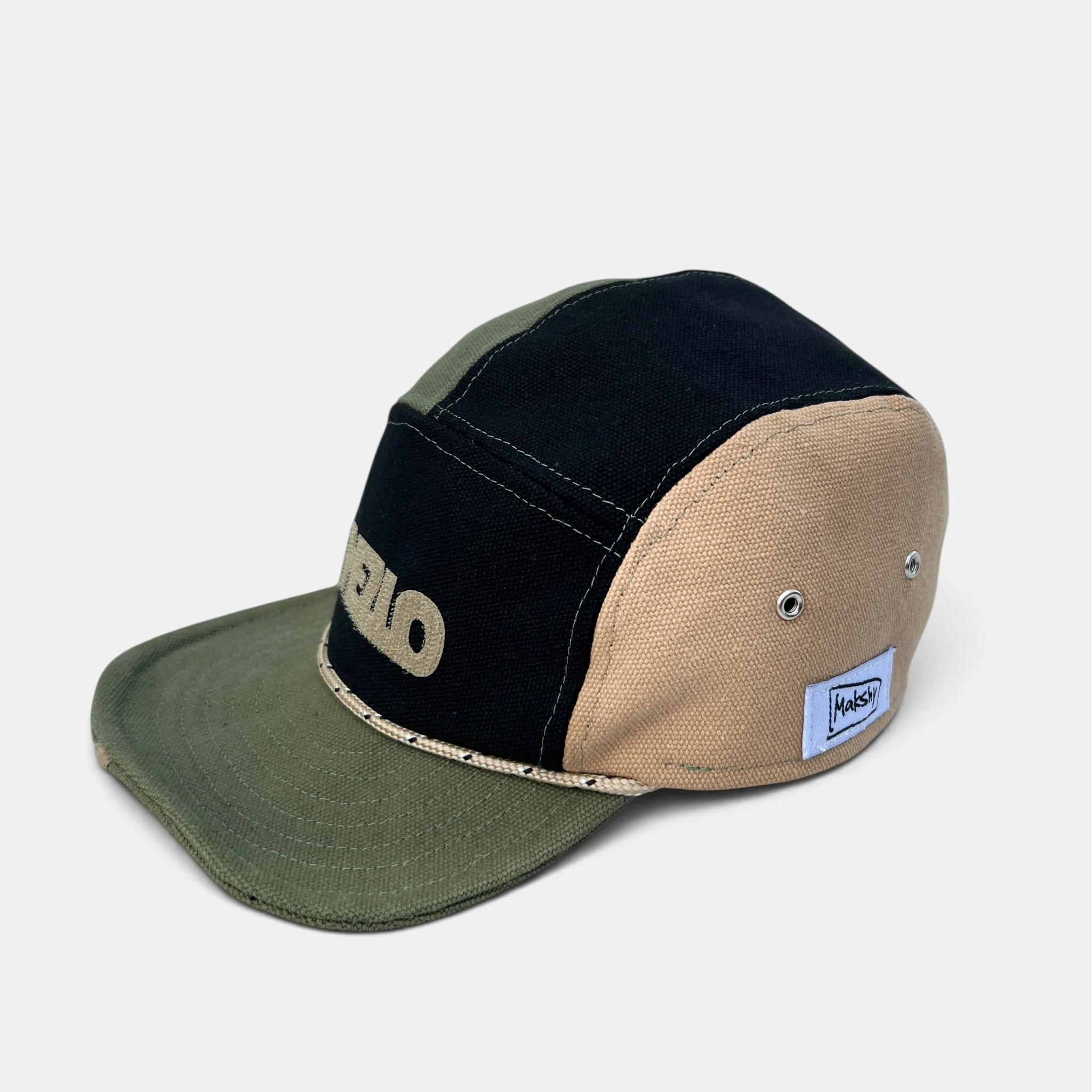 Side view of olive, black and beige cotton canvas five-panel cap with rope trim, metal eyelets and Makshy label.