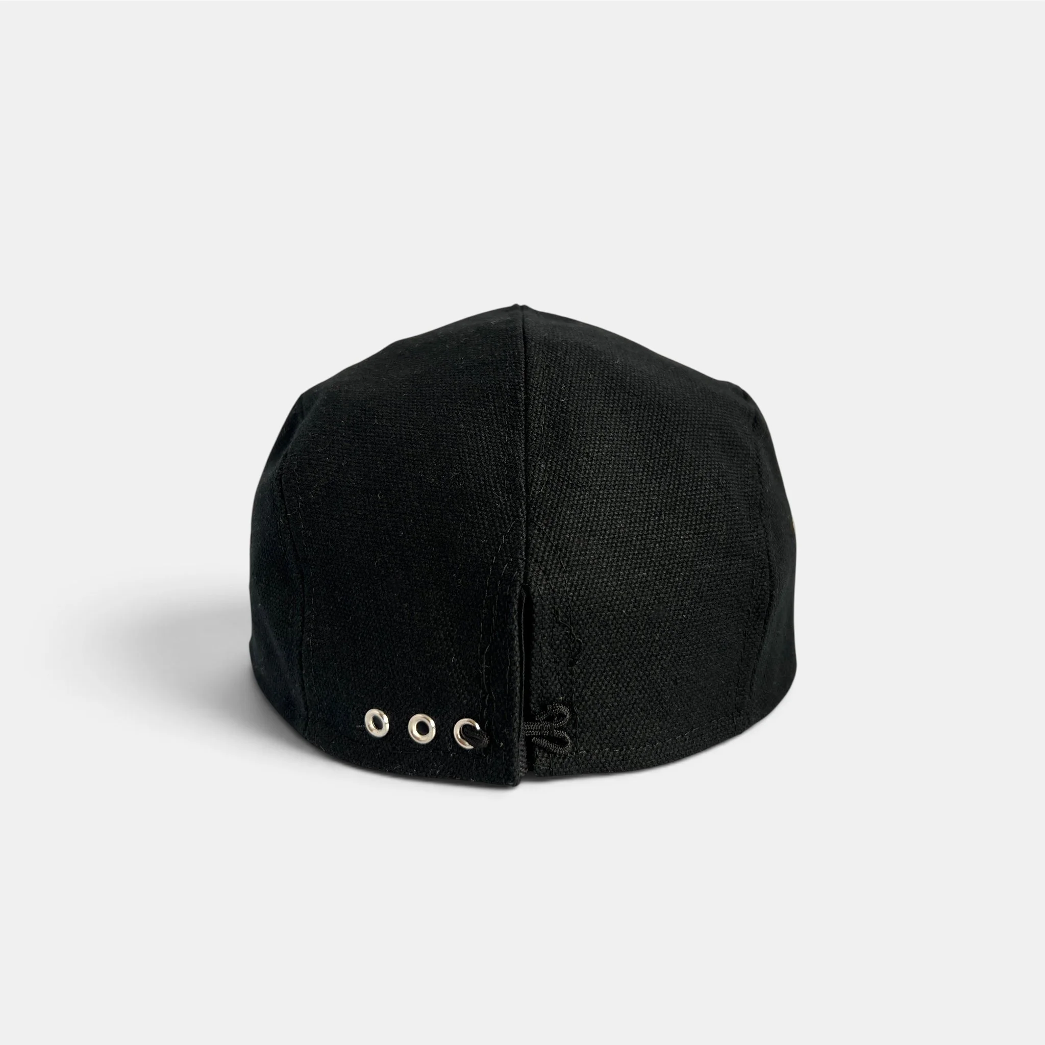 Back view of black cotton canvas five-panel cap with adjustable closure and metal eyelets.
