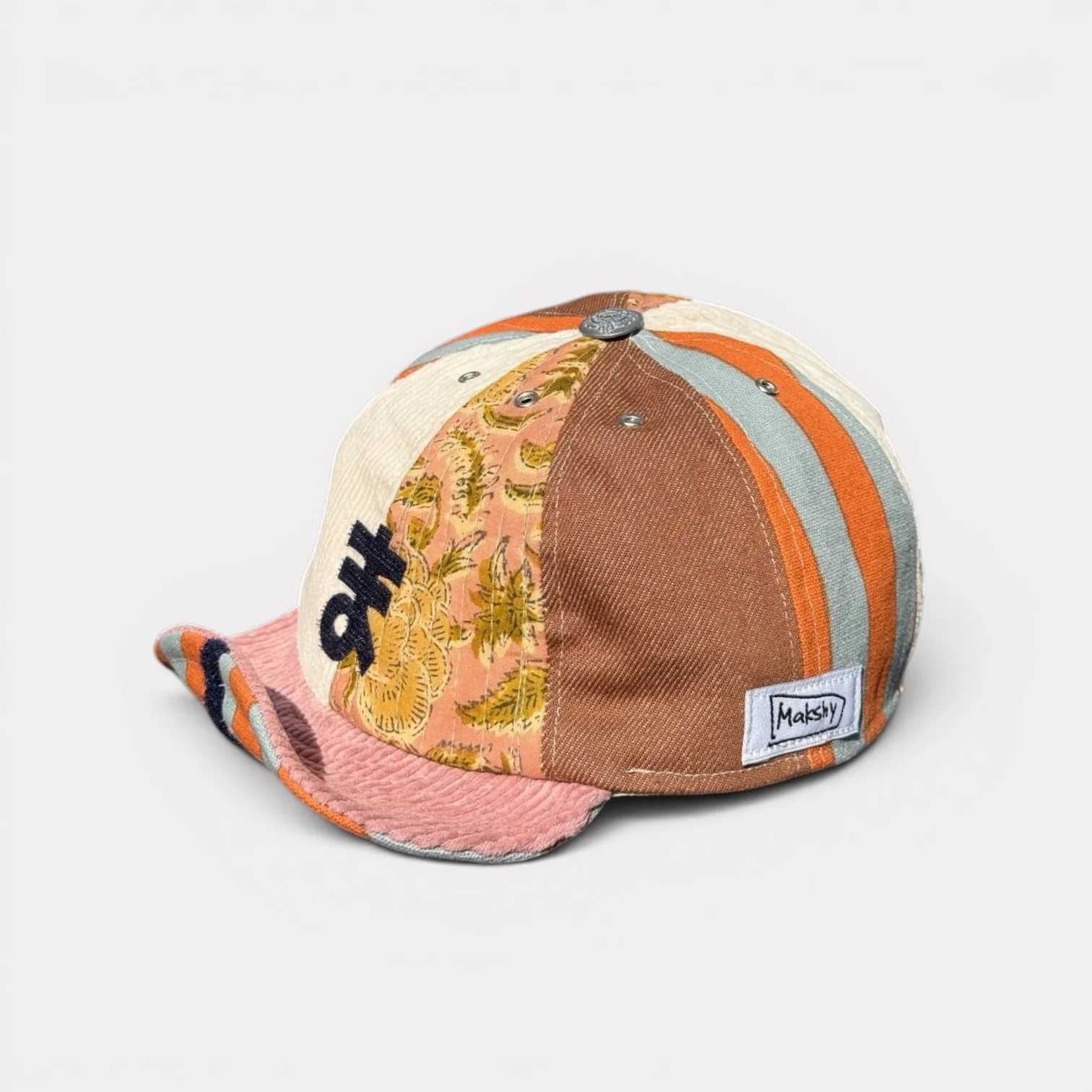 Mixed-panel cotton cap with roll-up visor, navy greeting motif, botanical-print panel and orange-and-turquoise striped accents.