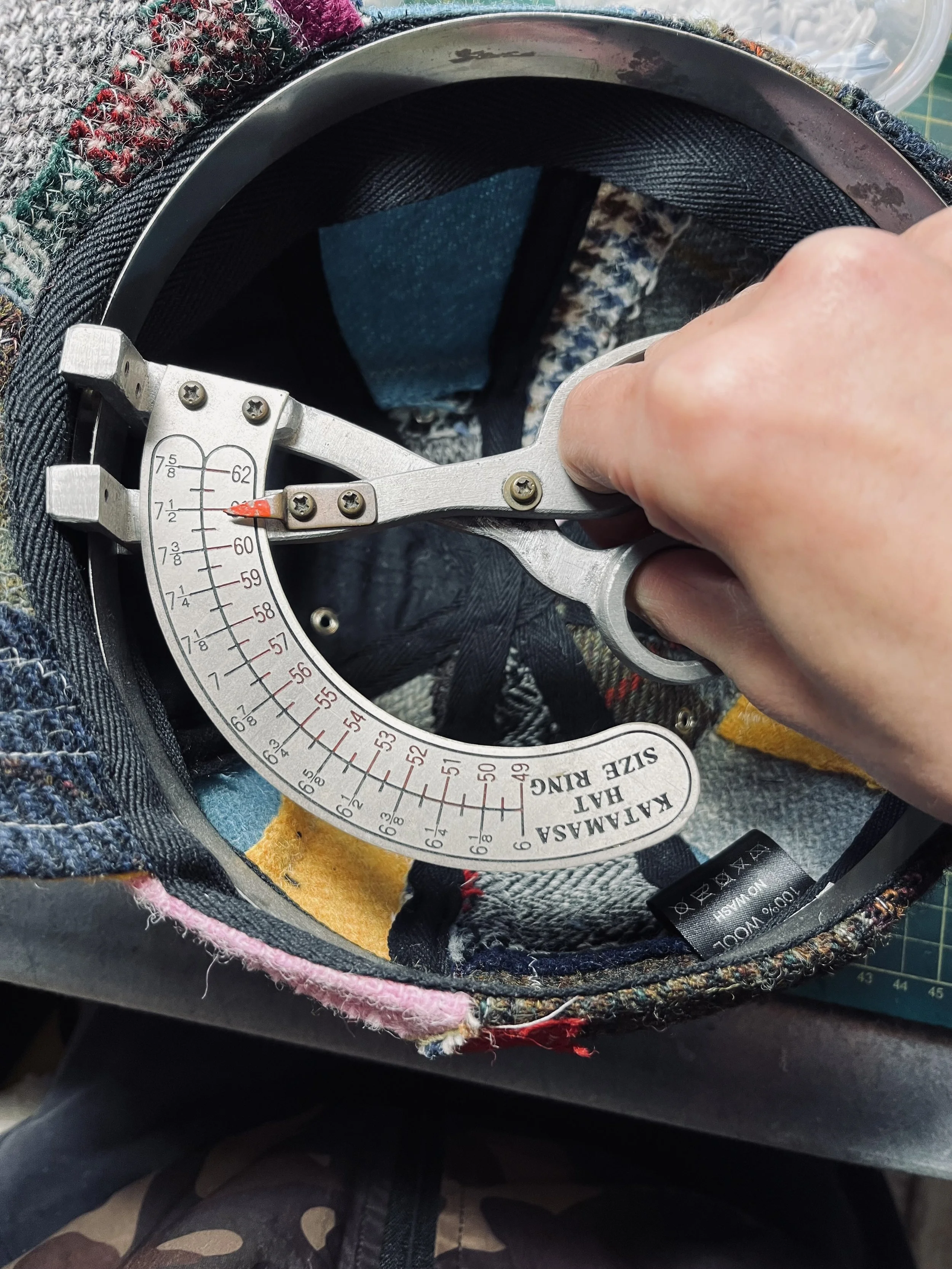 The meticulous craftsmanship of Makshy Millinery: a close-up shows a specialist tool measuring the final size of a bespoke patchwork cap made from authentic Harris tweed.