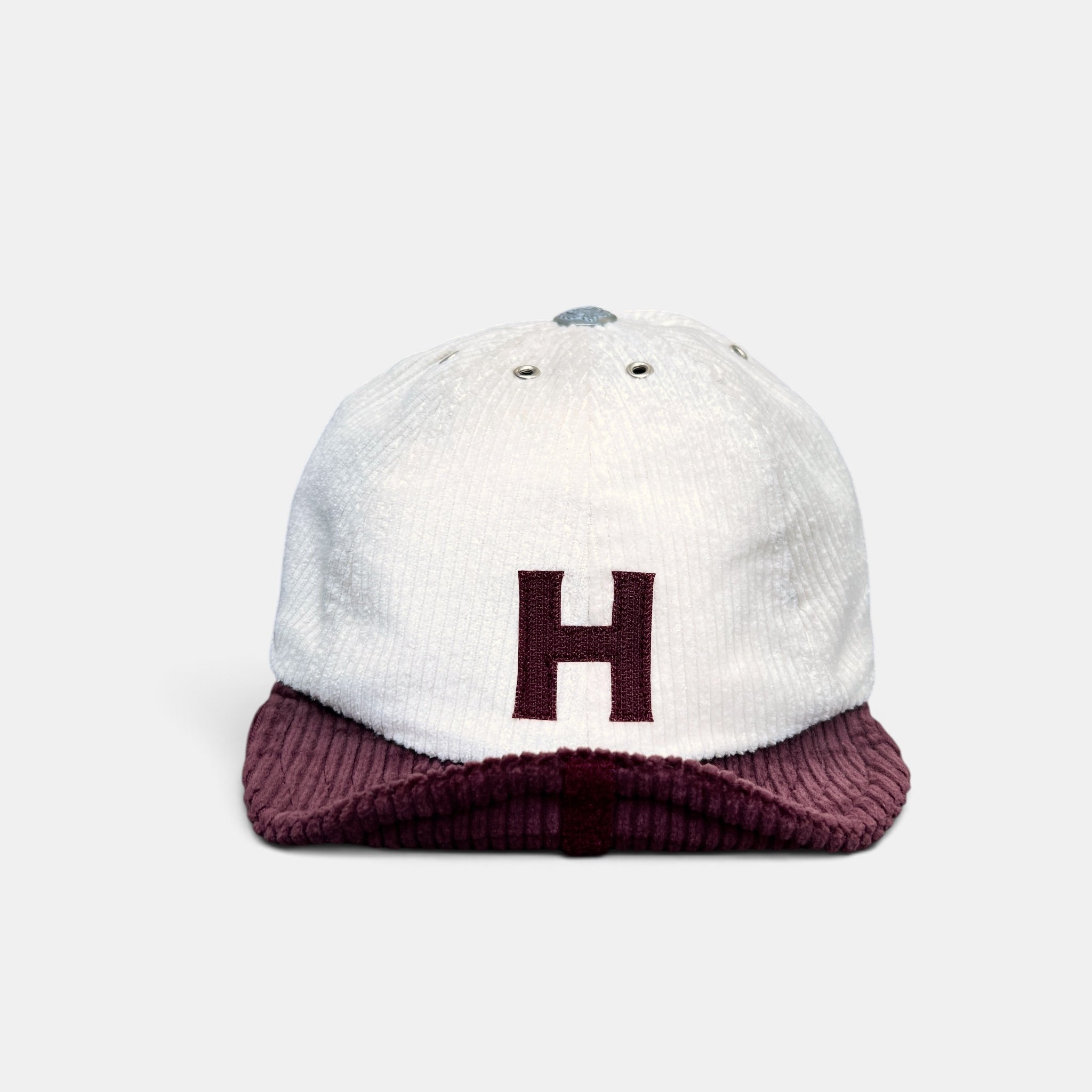 Front view of off-white eight-panel corduroy cap with burgundy roll-up visor and burgundy H initial motif.