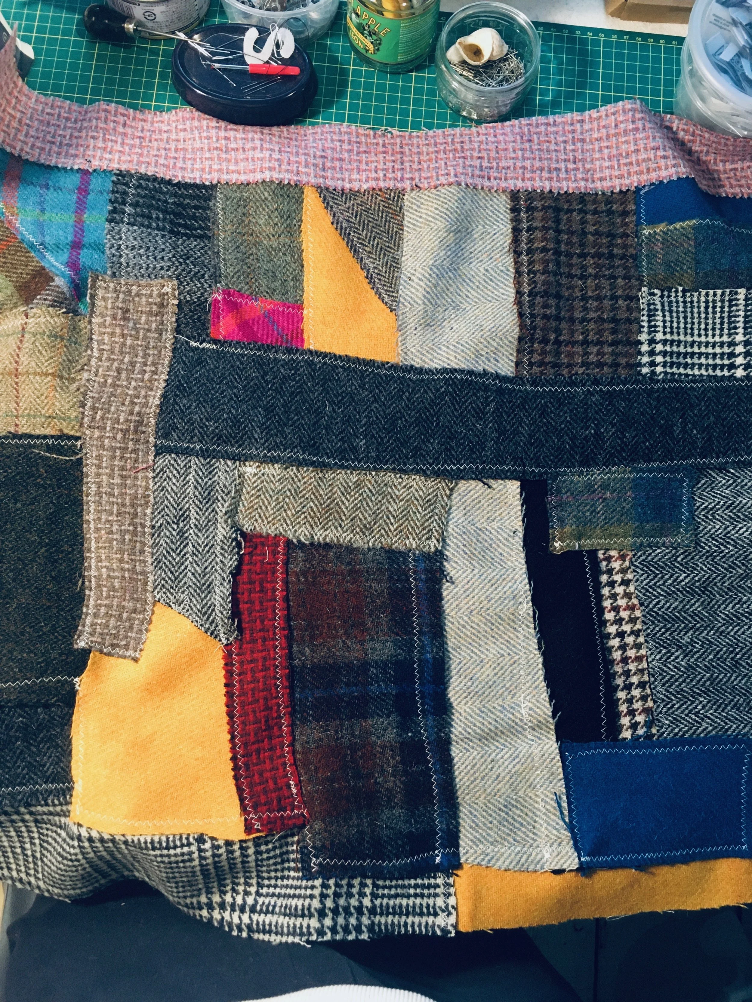 A patchwork quilt made of various fabric swatches in different colours and patterns, laid out on a work surface with sewing supplies around it.
